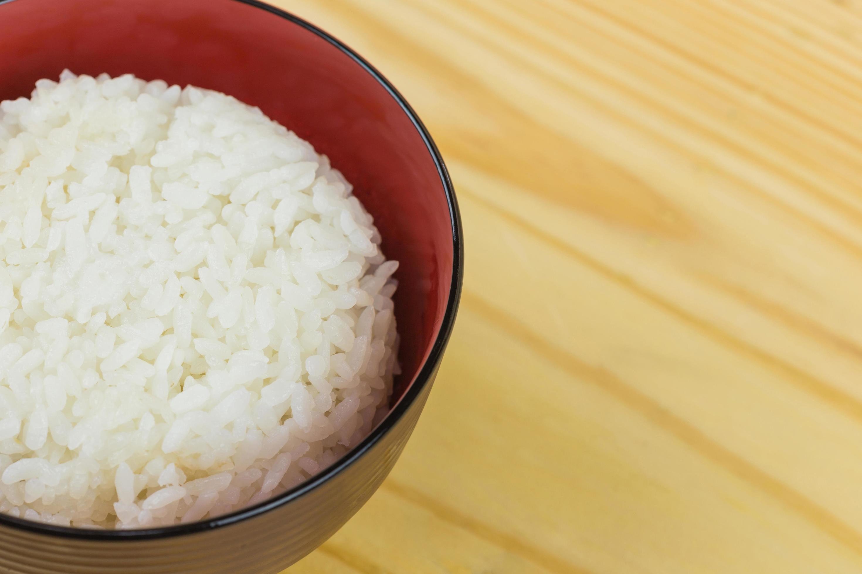 Cooked jasmine rice in white bowl on wooden table and dark background with copy space,high calories food,Top view. Stock Free