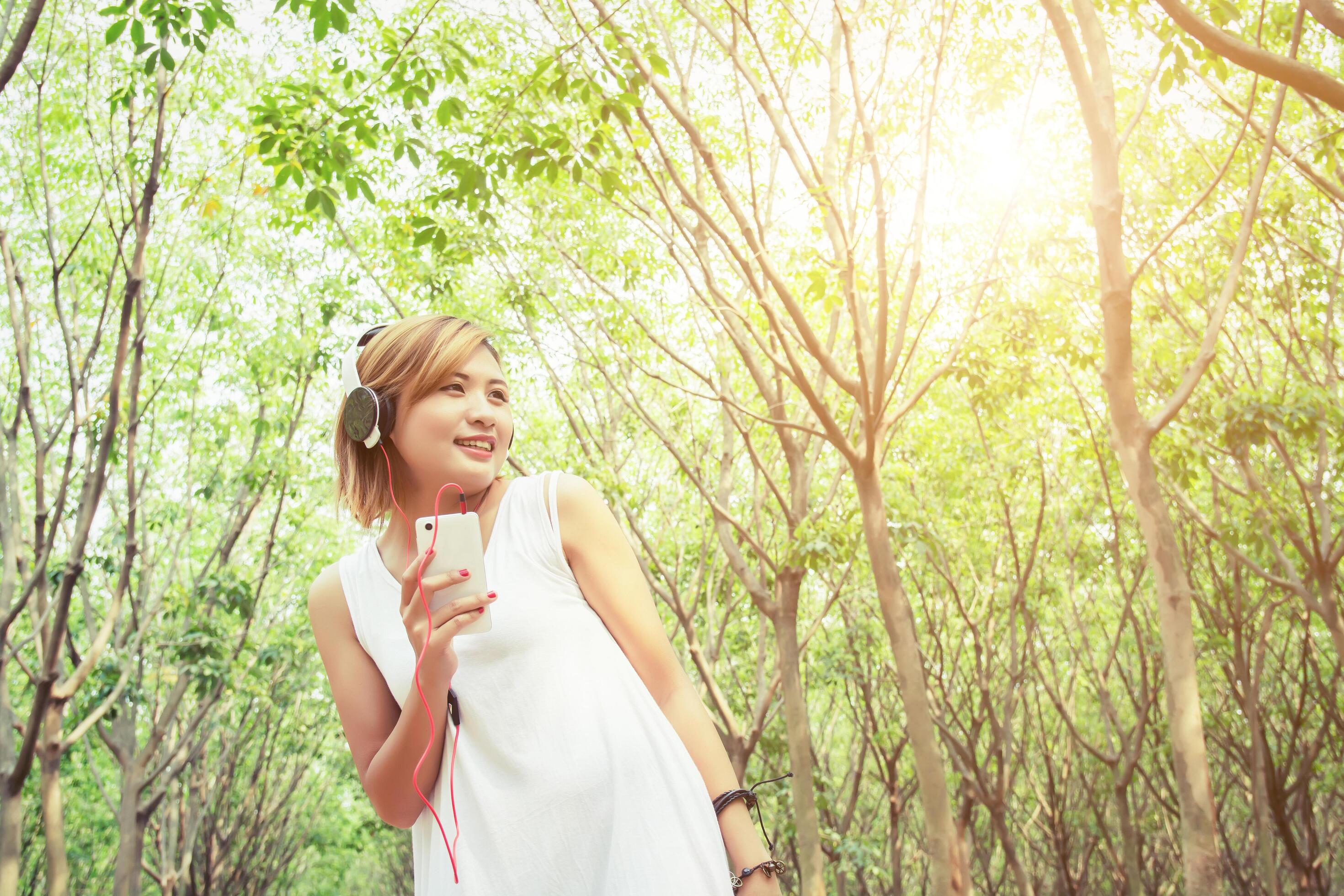 Lifestyle concept young asian woman listening enjoying music in forest Stock Free