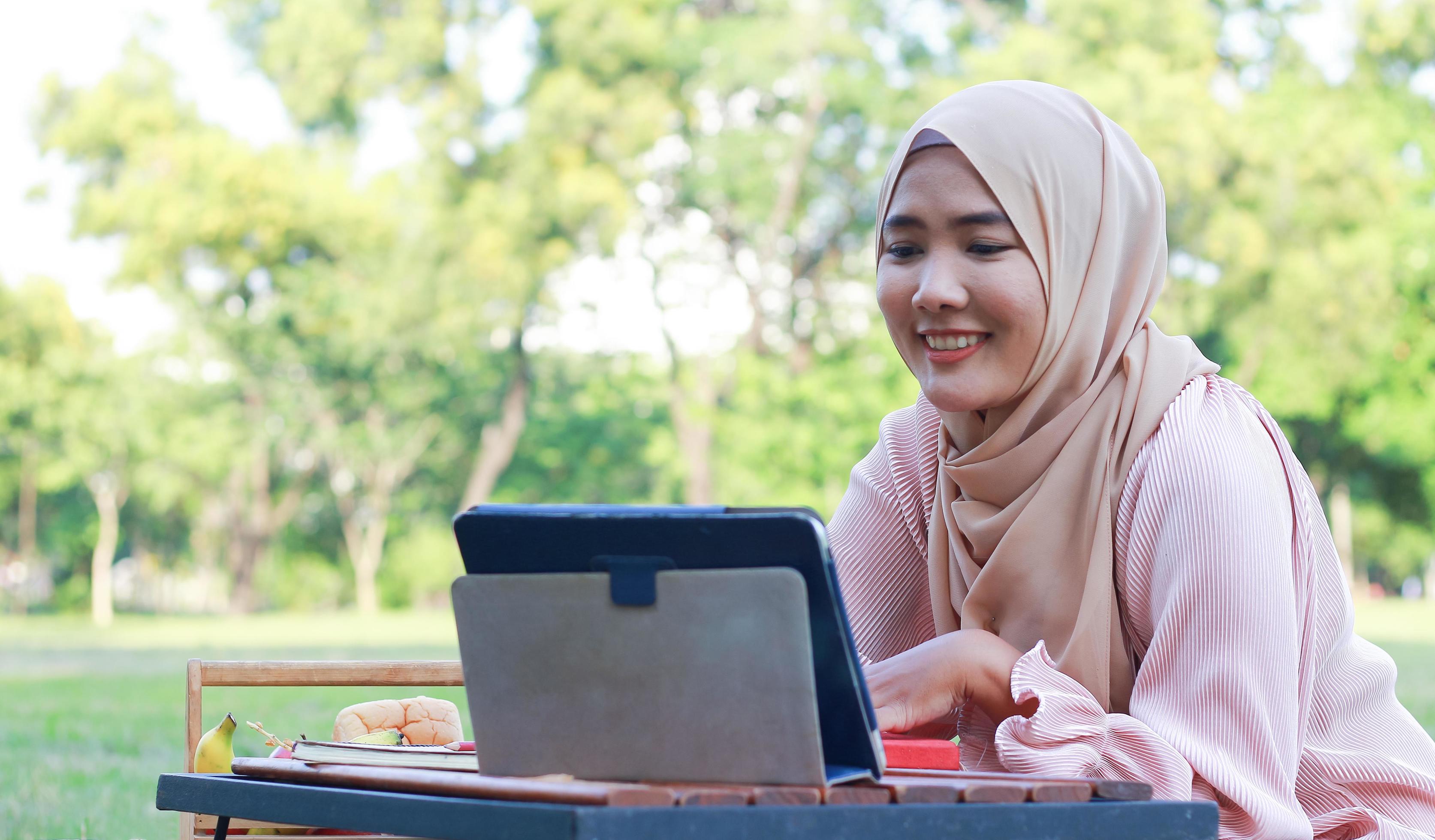 Beautiful Muslim girl sitting happily in the park. Muslim woman smiling in garden lawn. Lifestyle concept of a confident modern woman Stock Free