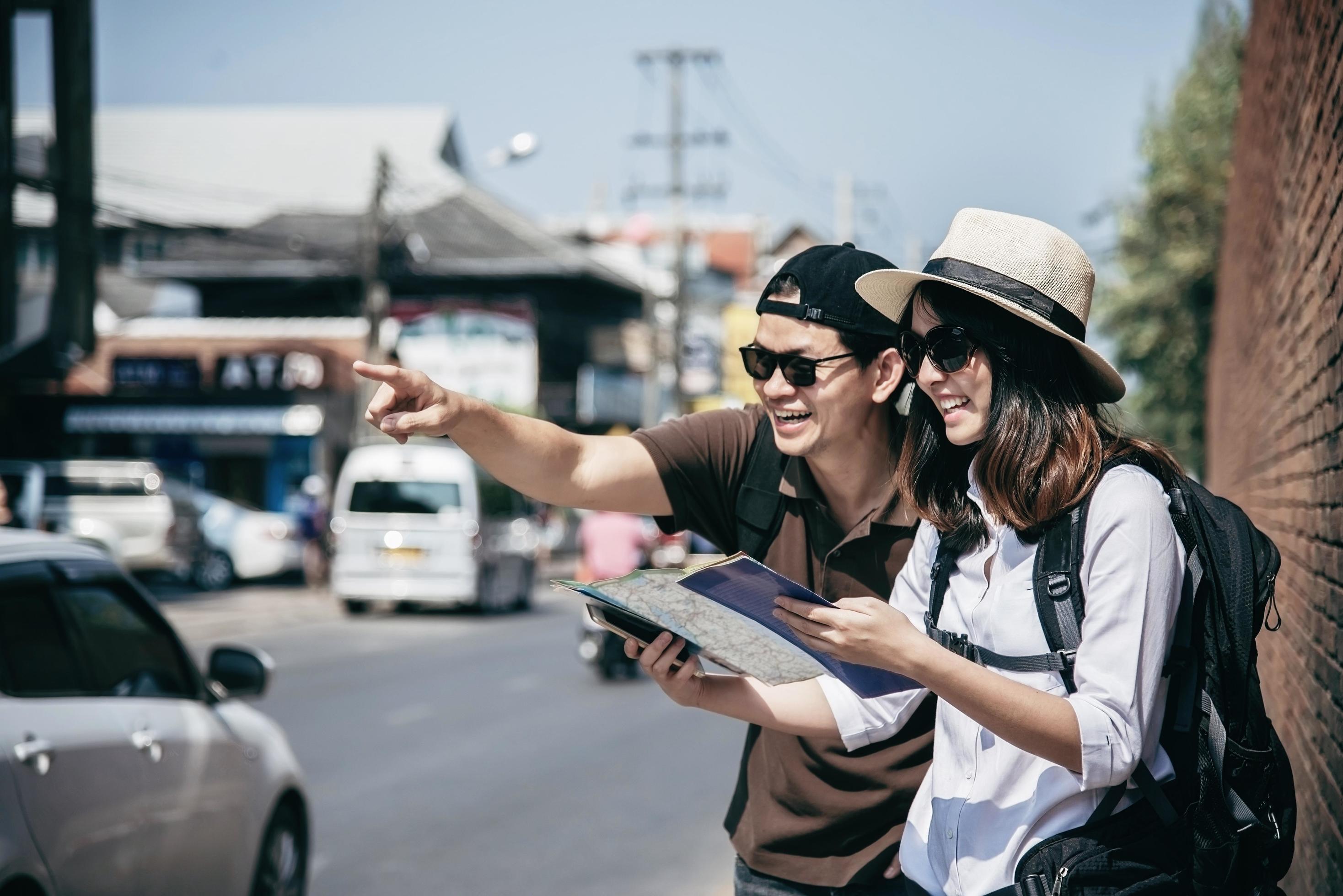 Asian backpack couple tourist holding city map crossing the road – travel people vacation lifestyle concept Stock Free