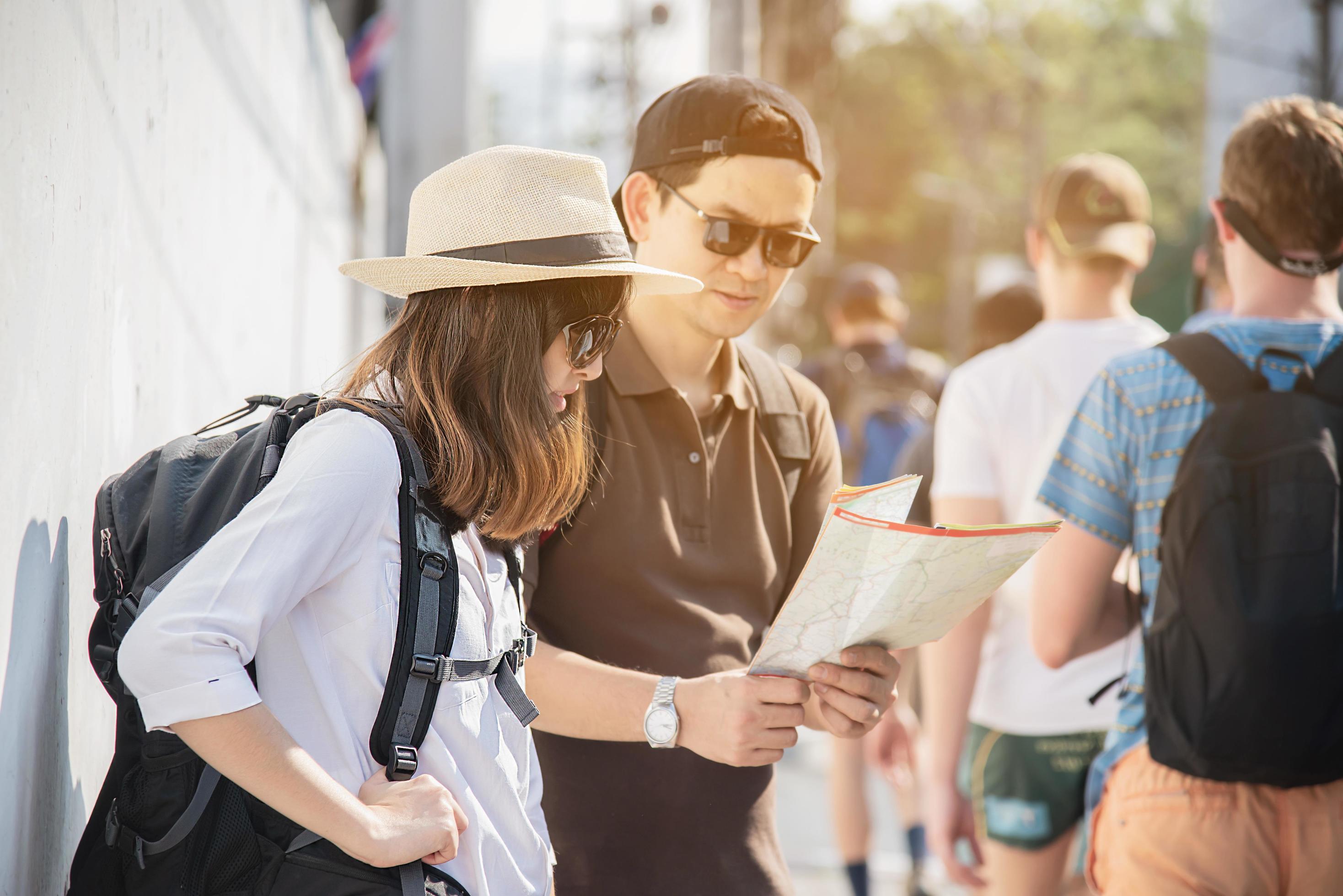 Asian backpack couple tourist holding city map crossing the road – travel people vacation lifestyle concept Stock Free