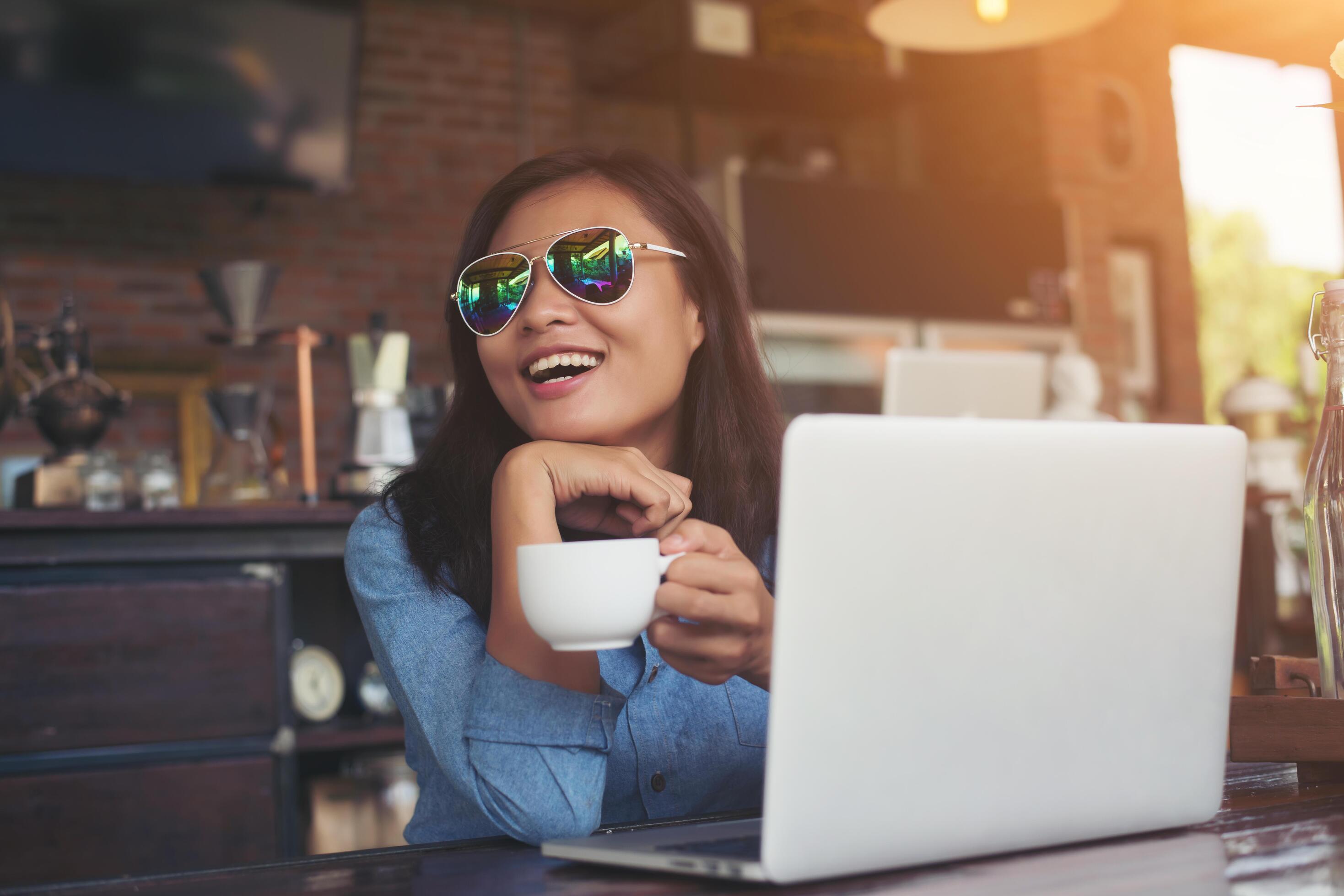 Pretty young hipster woman sitting in a cafe with her laptop, looked away and smiled happy, Relaxing with holiday, Woman lifestyle concept. Stock Free