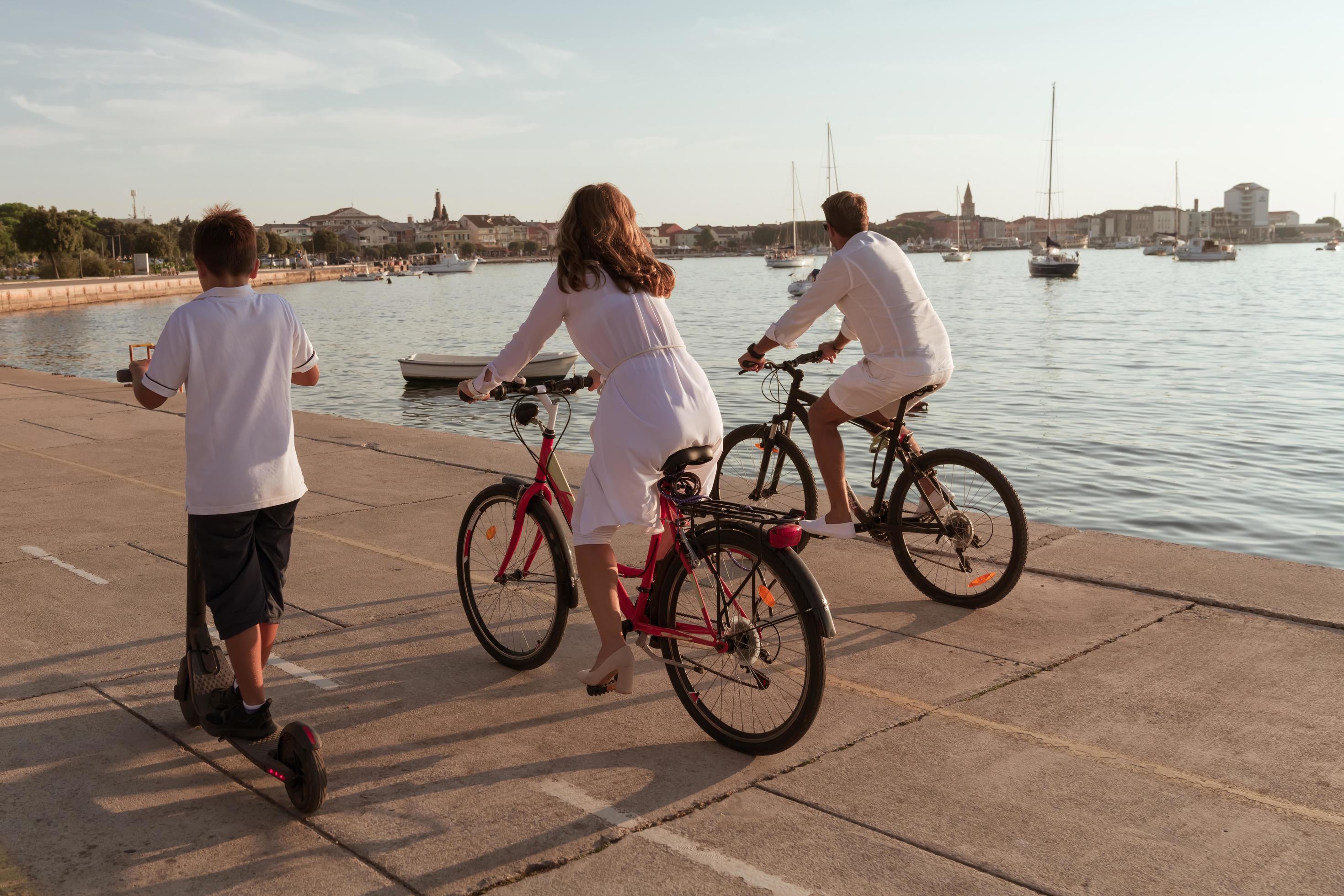 Happy family enjoying a beautiful morning by the sea together, parents riding a bike and their son riding an electric scooter. Selective focus Stock Free