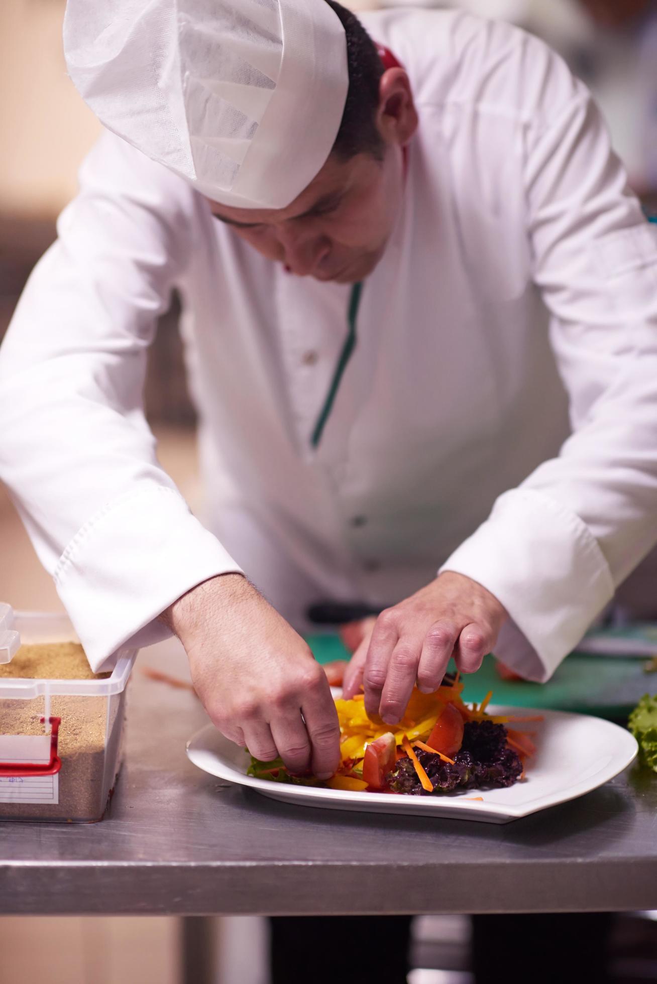 chef in hotel kitchen preparing and decorating food Stock Free