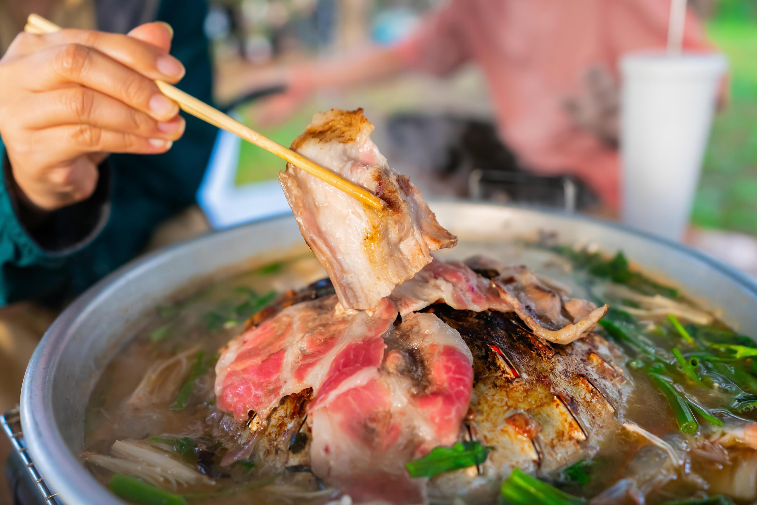 Korean BBQ or MOOKATA with sliced pork and vegetable soup, People hand using chopsticks grilled dinner the family. picnic outdoor. Close up Stock Free