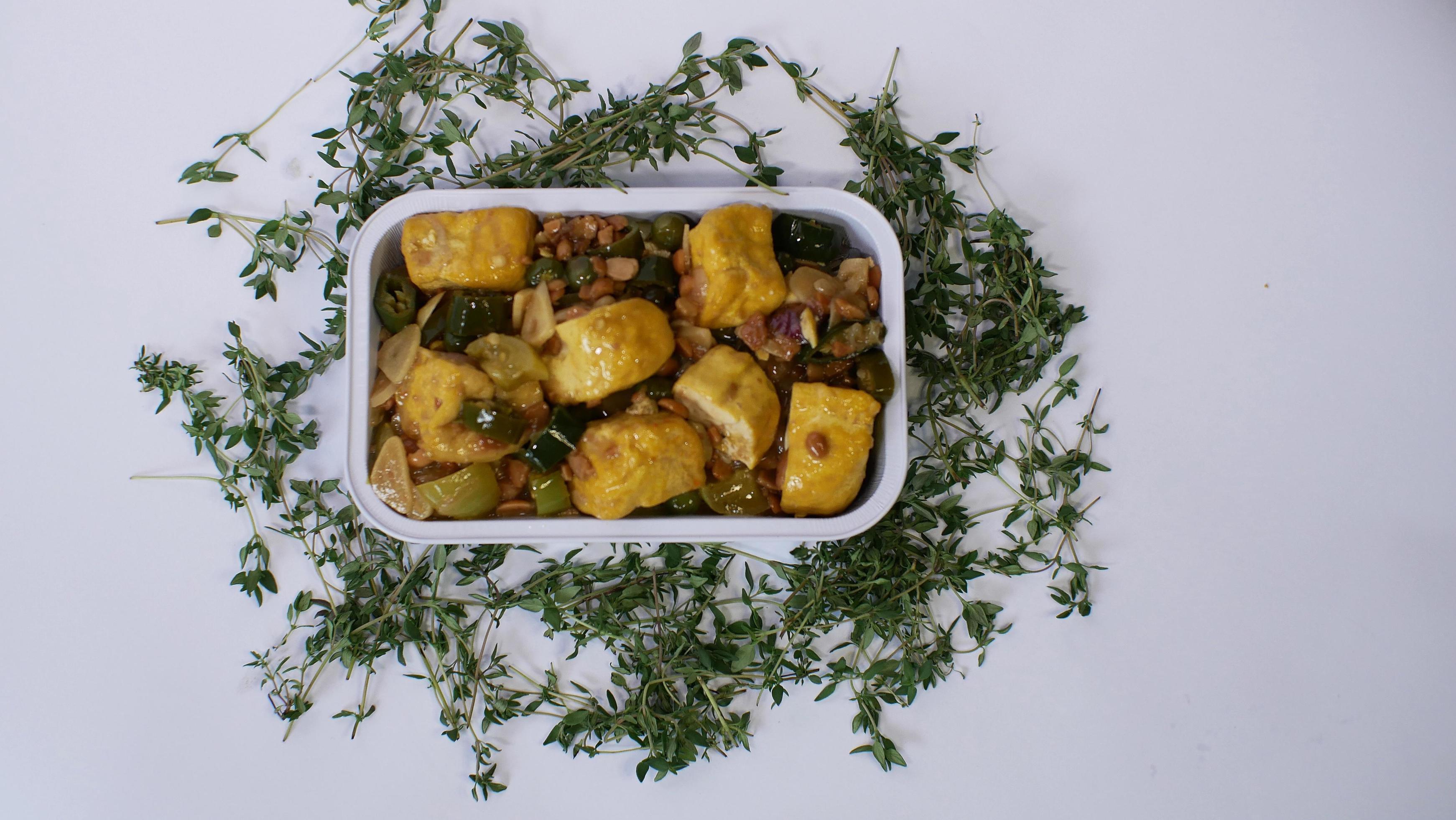 Vegetable tofu with yellow spices Indonesian food served in an aluminum holder with a white background with a few green leaves around it Stock Free