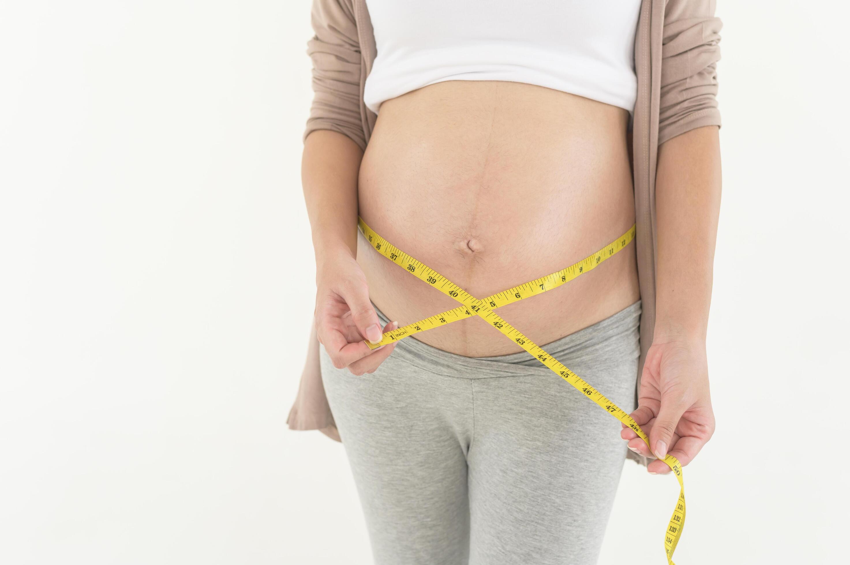 
									Pregnant woman using measuring tape to check size of belly pregnancy and baby development Stock Free