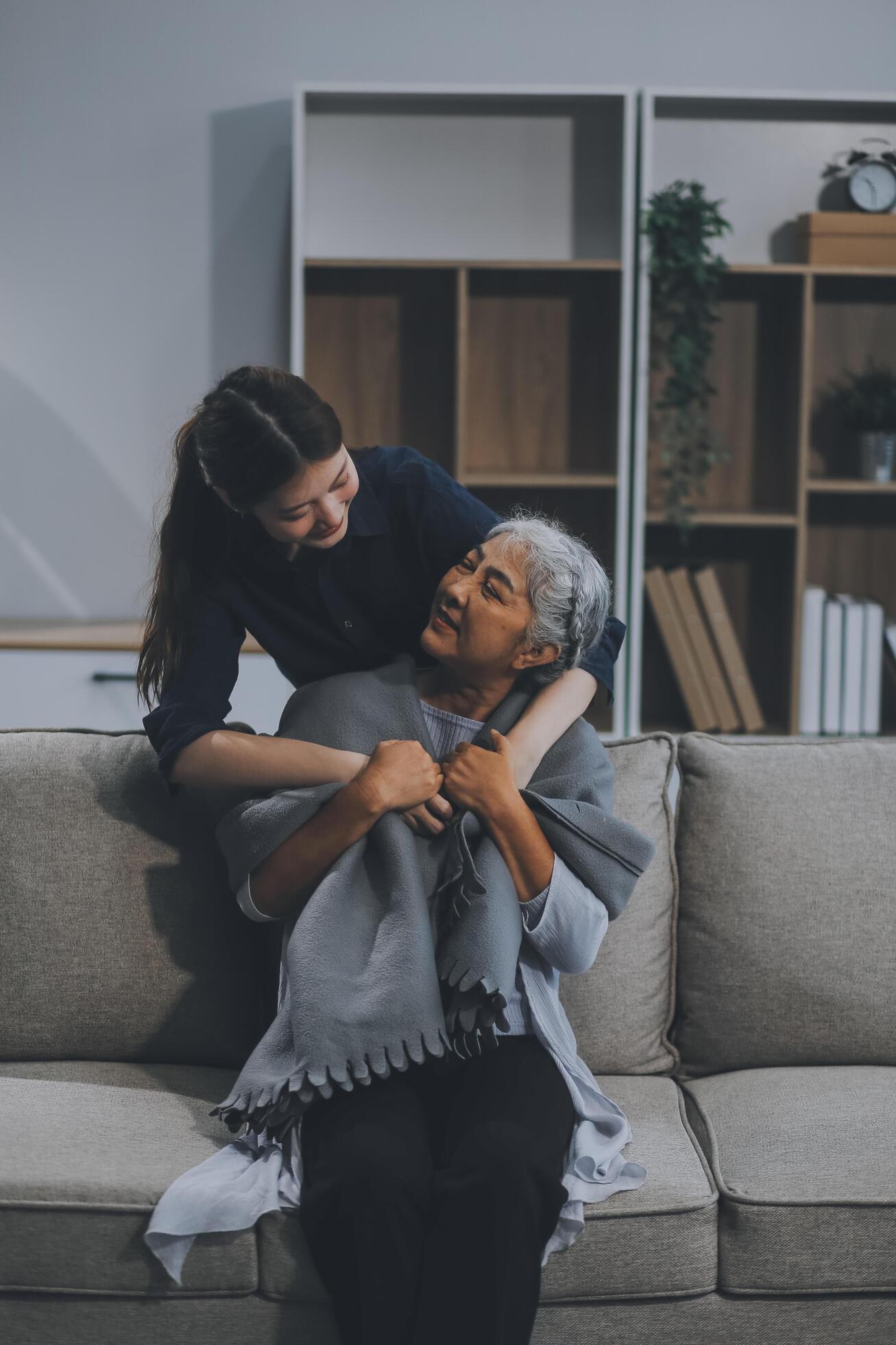 happy family Granddaughter takes care of her grandmother with warm cloths sitting on the sofa. Stock Free