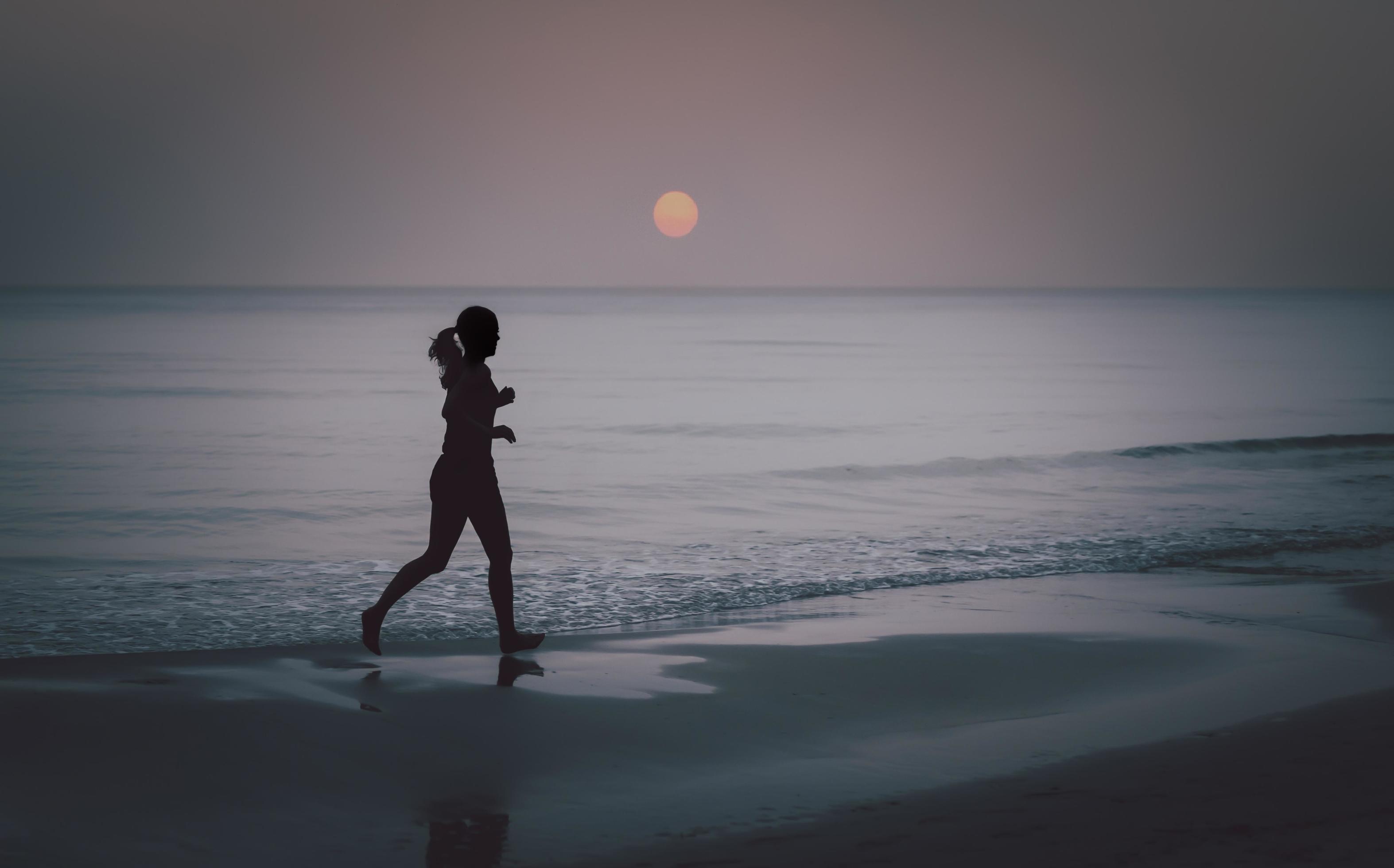 Silhouette of barefoot woman running on the beach at sunrise. Stock Free