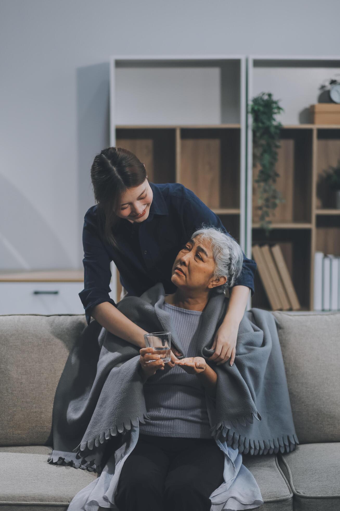 happy family Granddaughter takes care of her grandmother with warm cloths sitting on the sofa. Stock Free