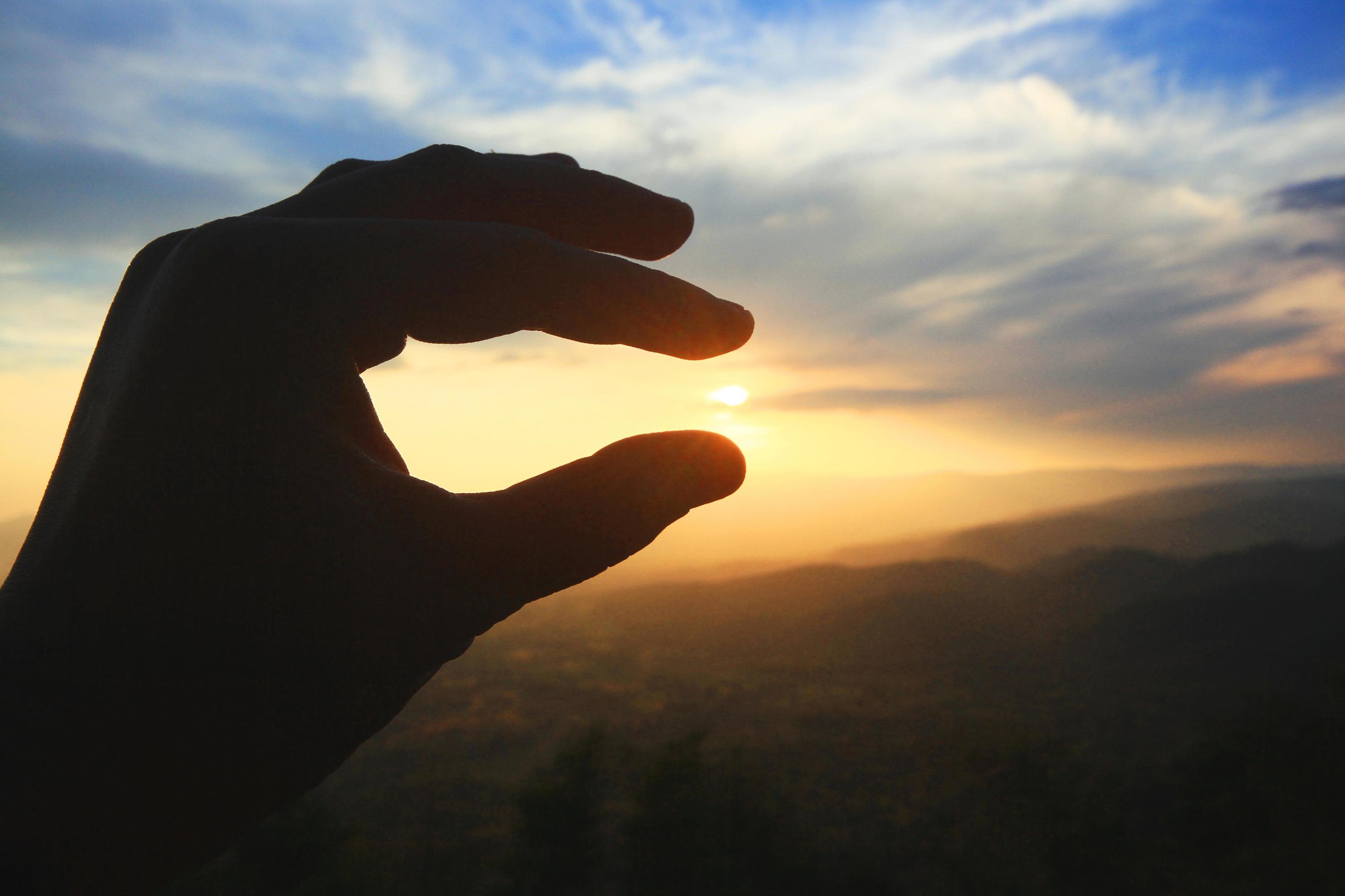 Beautiful silhouette hand holding on sun and sunset on the mountain. Power and hope Concept. Stock Free