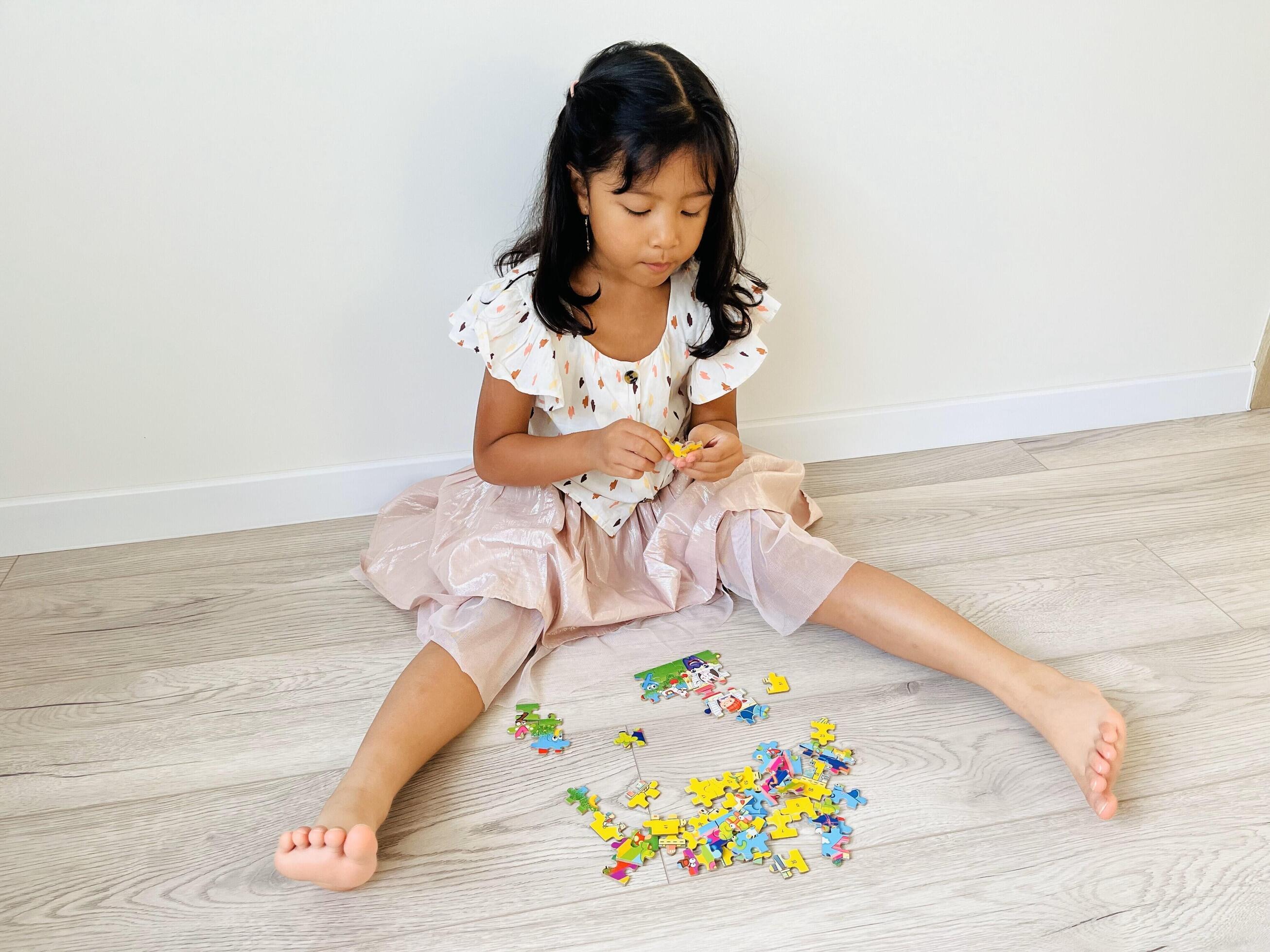 A five year old Asian girl is sitting on the floor with a wooden motif playing with jigsaw puzzle Stock Free