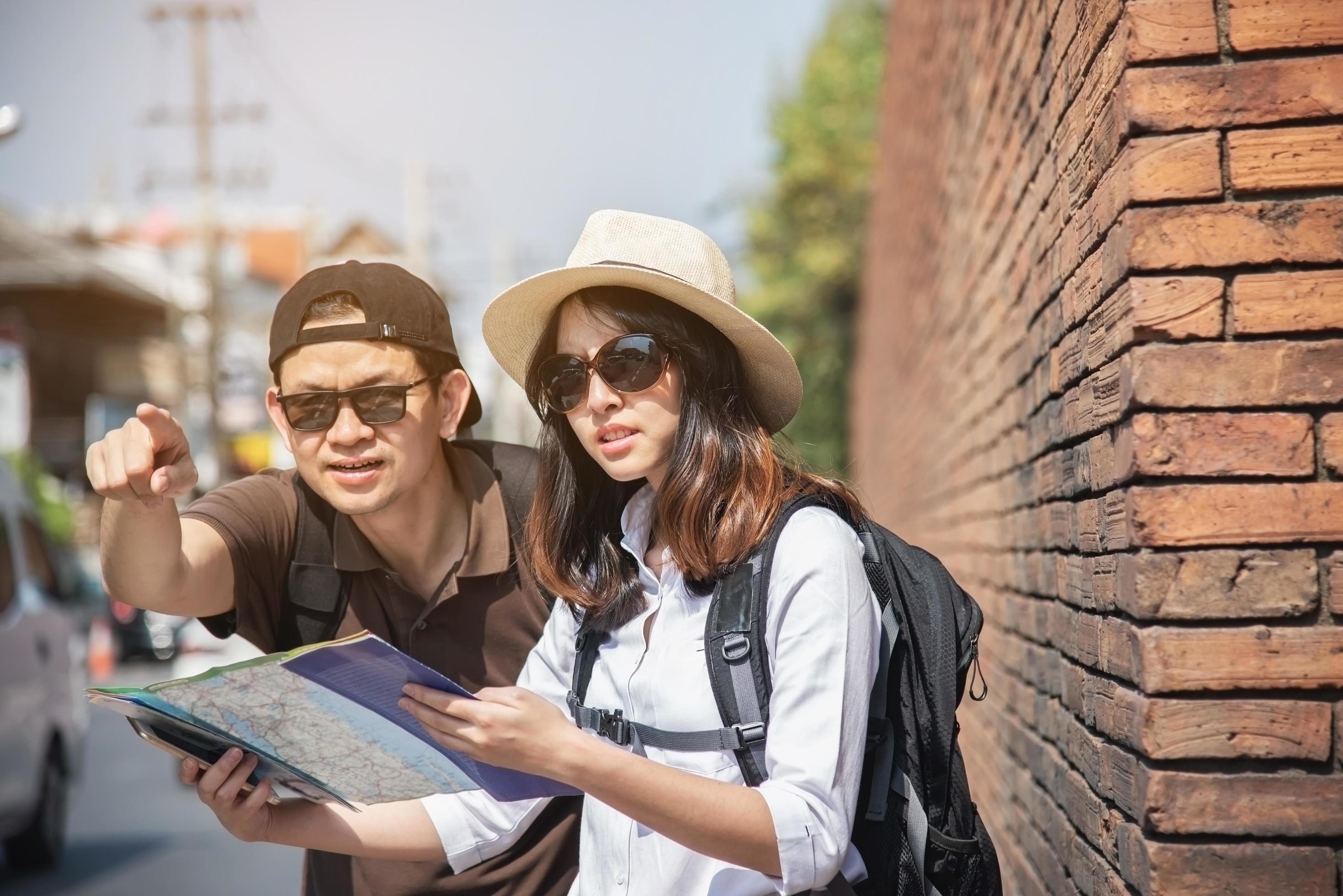 Asian backpack couple tourist holding city map crossing the road – travel people vacation lifestyle concept Stock Free