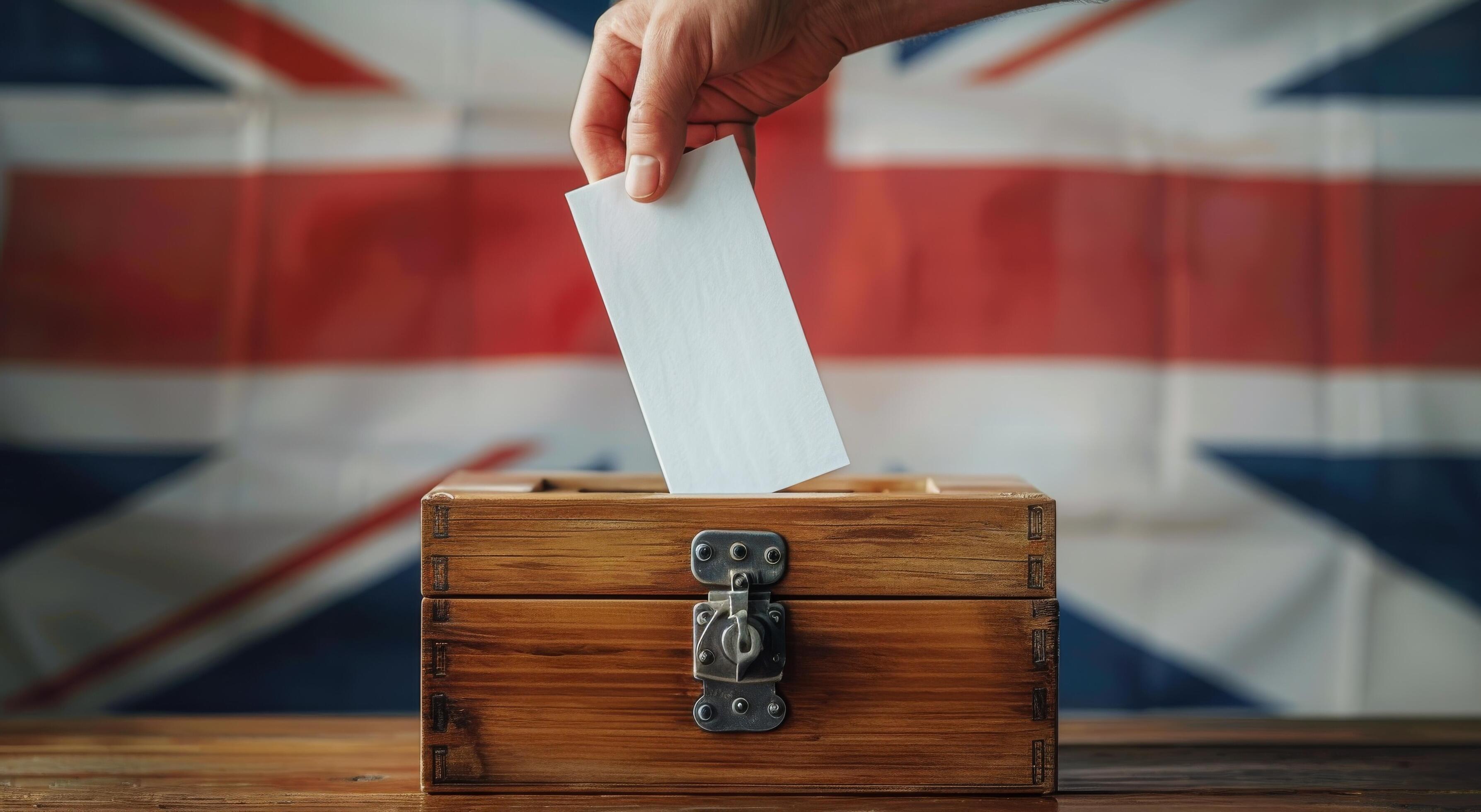 Hand Placing Ballot in Wooden Box With UK Flag Background Stock Free