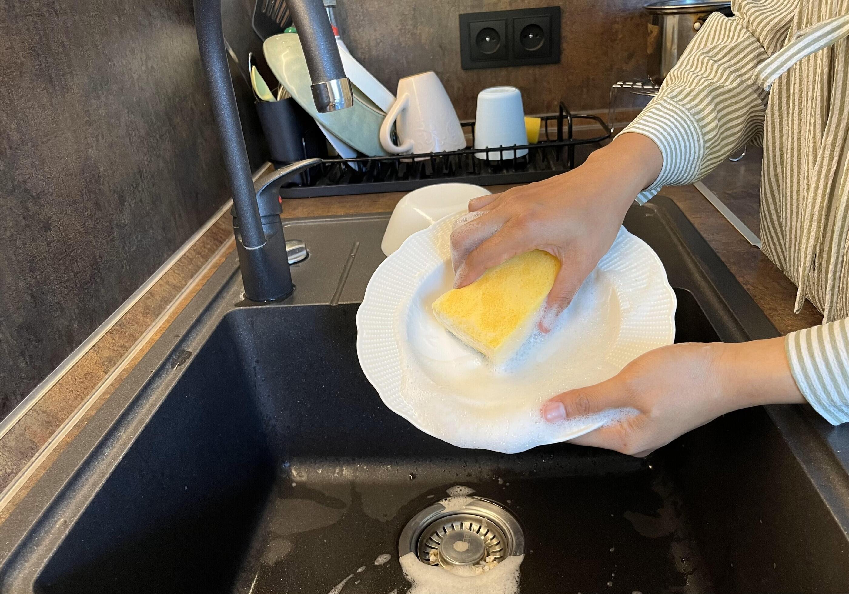 Close up of woman housewife is doing the dishes at home kitchen by using wash sponge and dishwashing soap. Clean the plate Stock Free