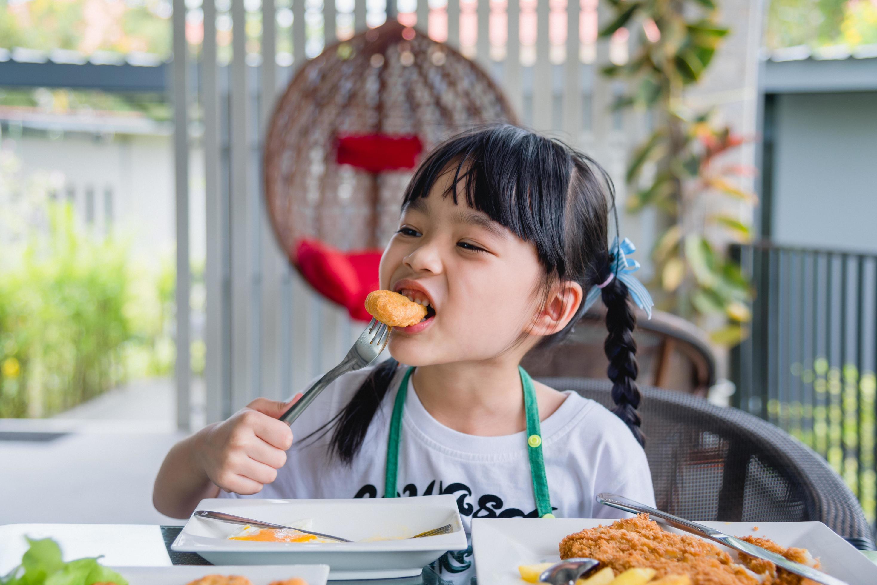 Asian young girl Eating Chicken nuggets fast food on table. Stock Free