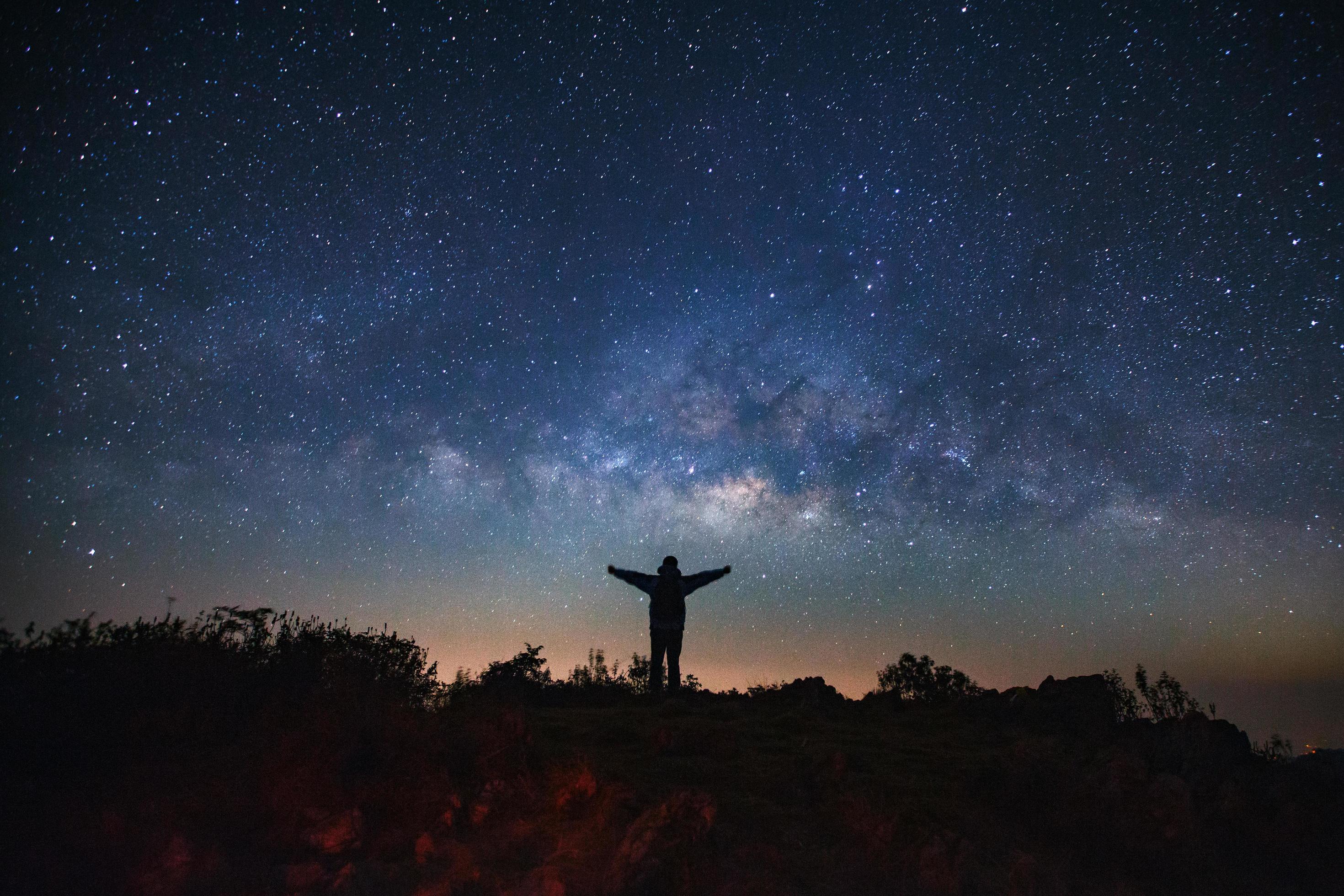 Landscape with milky way galaxy, Starry night sky with stars and silhouette of a standing sporty man with raised up arms on high mountain. Stock Free