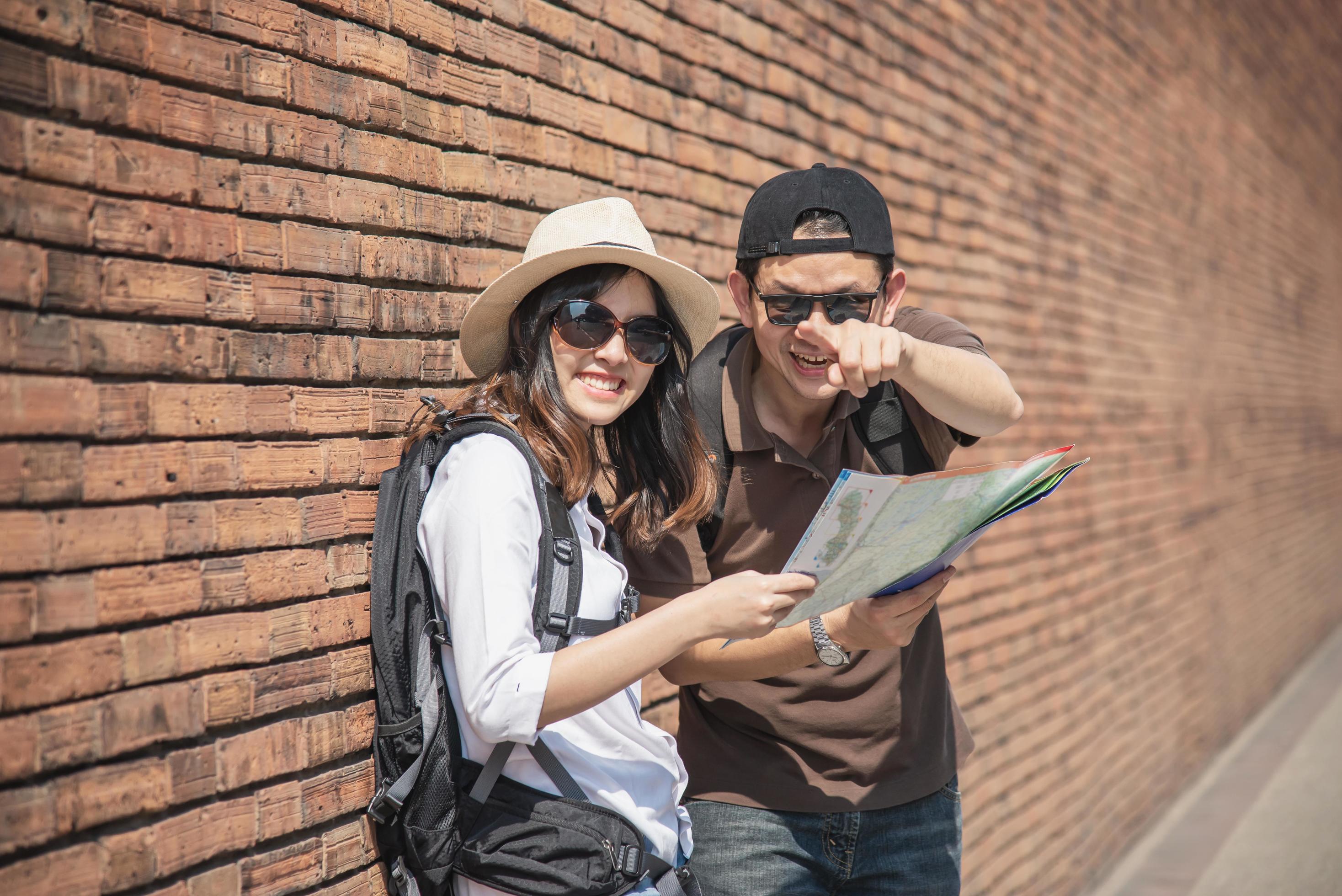 Asian backpack couple tourist holding city map crossing the road – travel people vacation lifestyle concept Stock Free