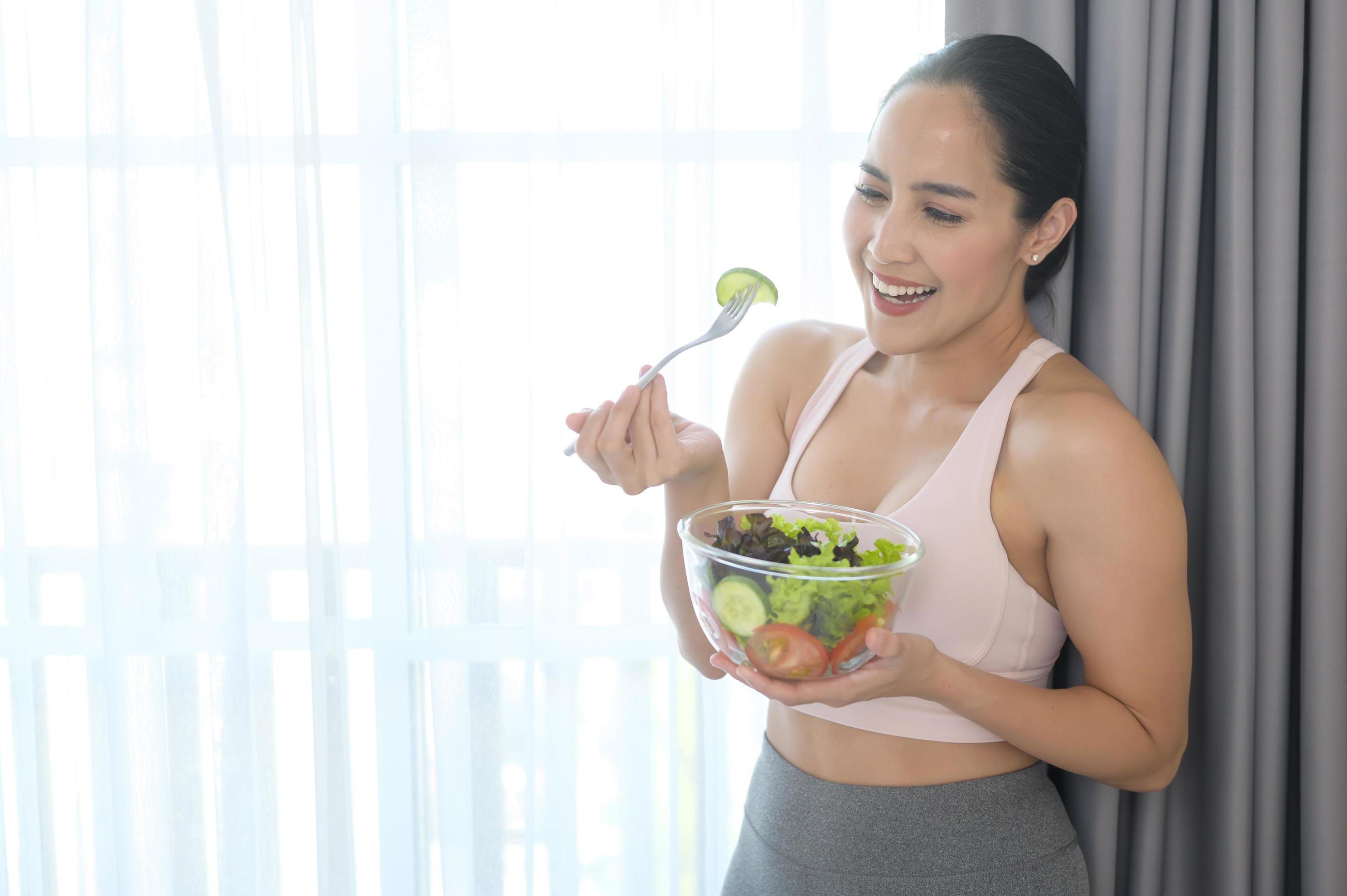 Fit young woman having salad after work out at home, sport and healthy lifestyle concept. Stock Free