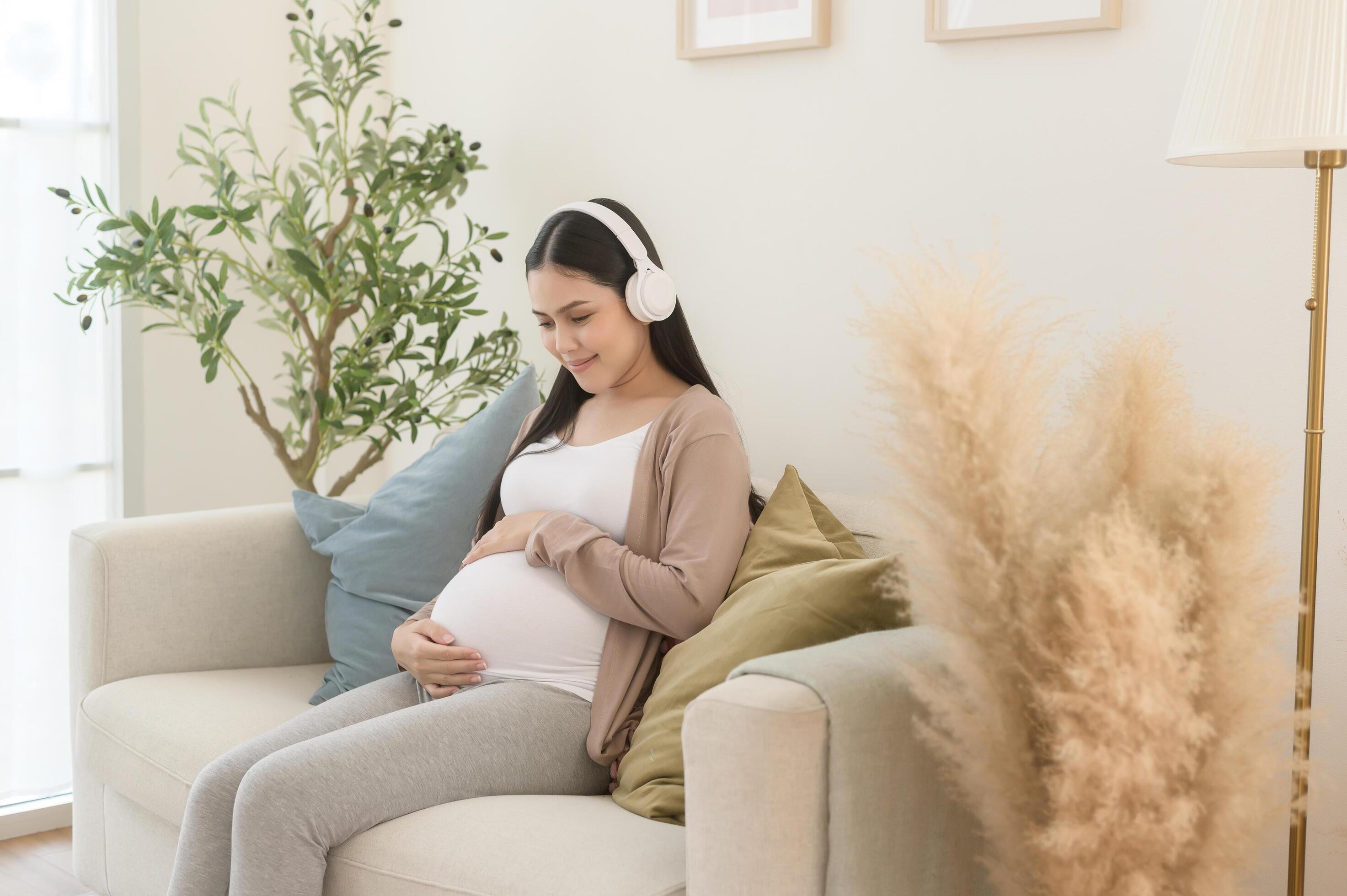 Happy pregnant woman with headphones listening to mozart music and lying on sofa, pregnancy concept Stock Free