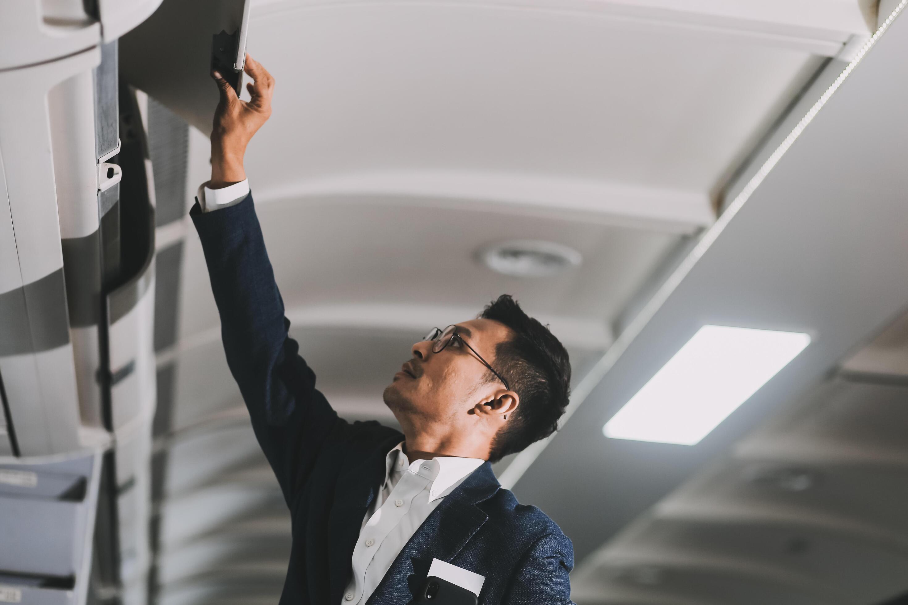 Handsome Asian male passenger takes his carry-on luggage out of the overhead locker after landing at his destination. transportation concept Stock Free