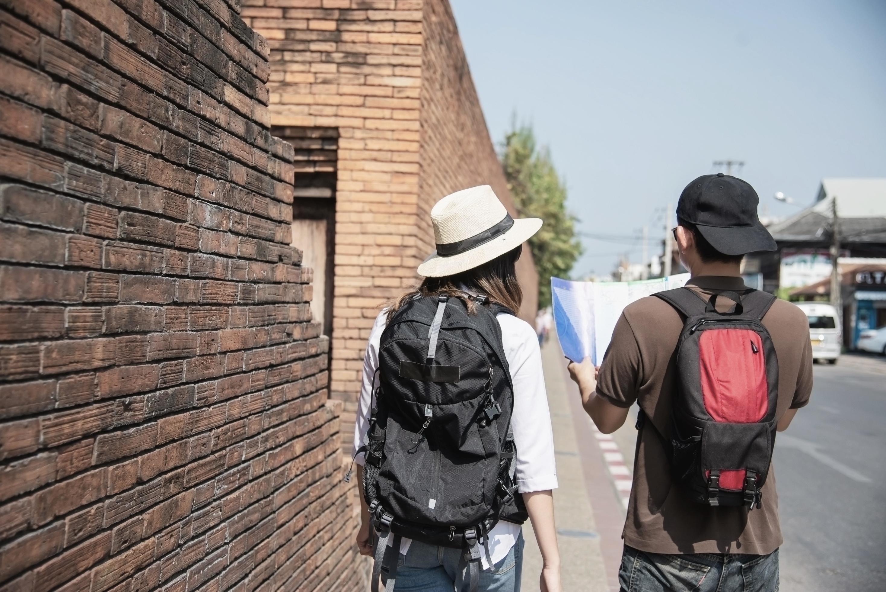 Asian backpack couple tourist holding city map crossing the road – travel people vacation lifestyle concept Stock Free