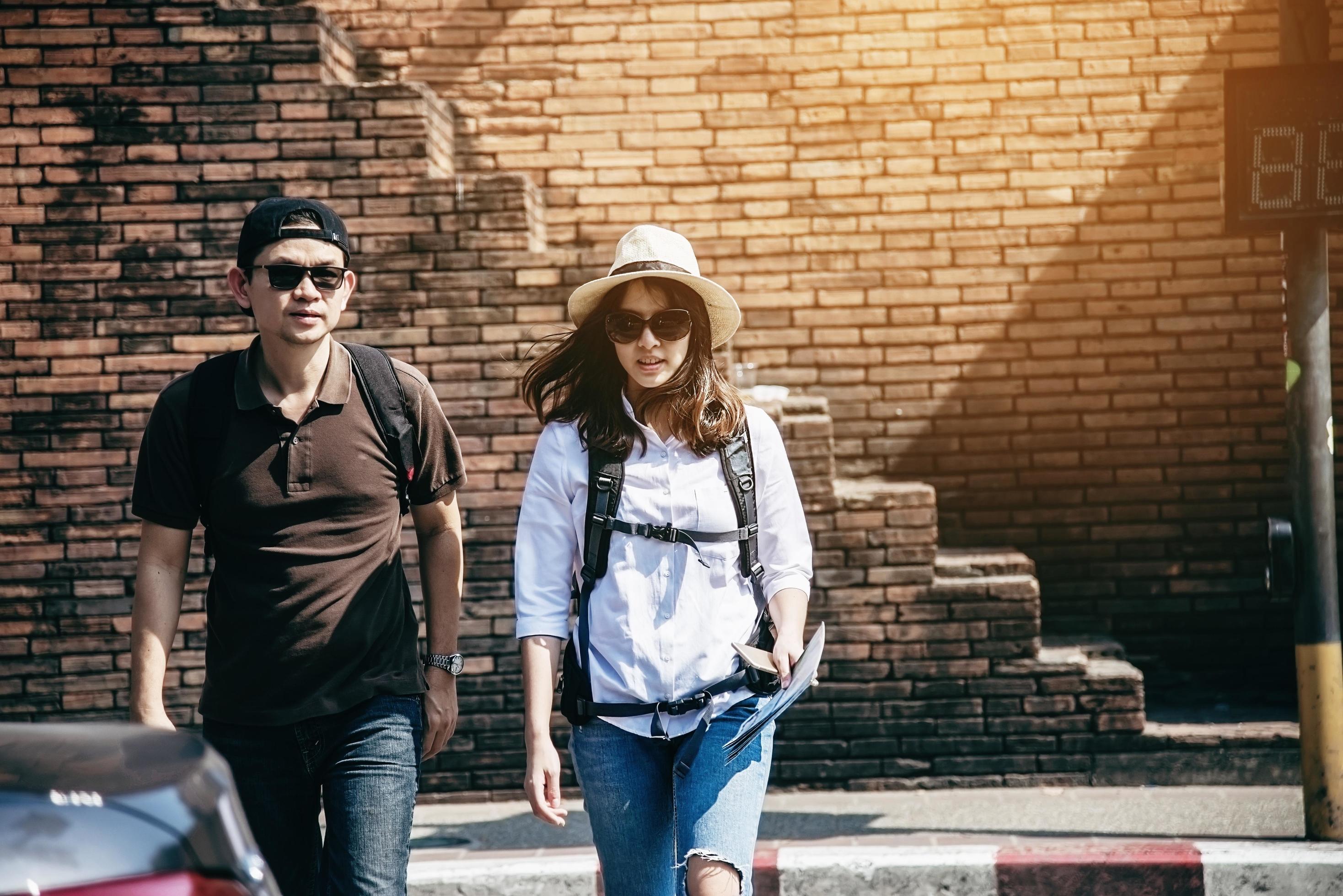 Asian backpack couple tourist holding city map crossing the road – travel people vacation lifestyle concept Stock Free