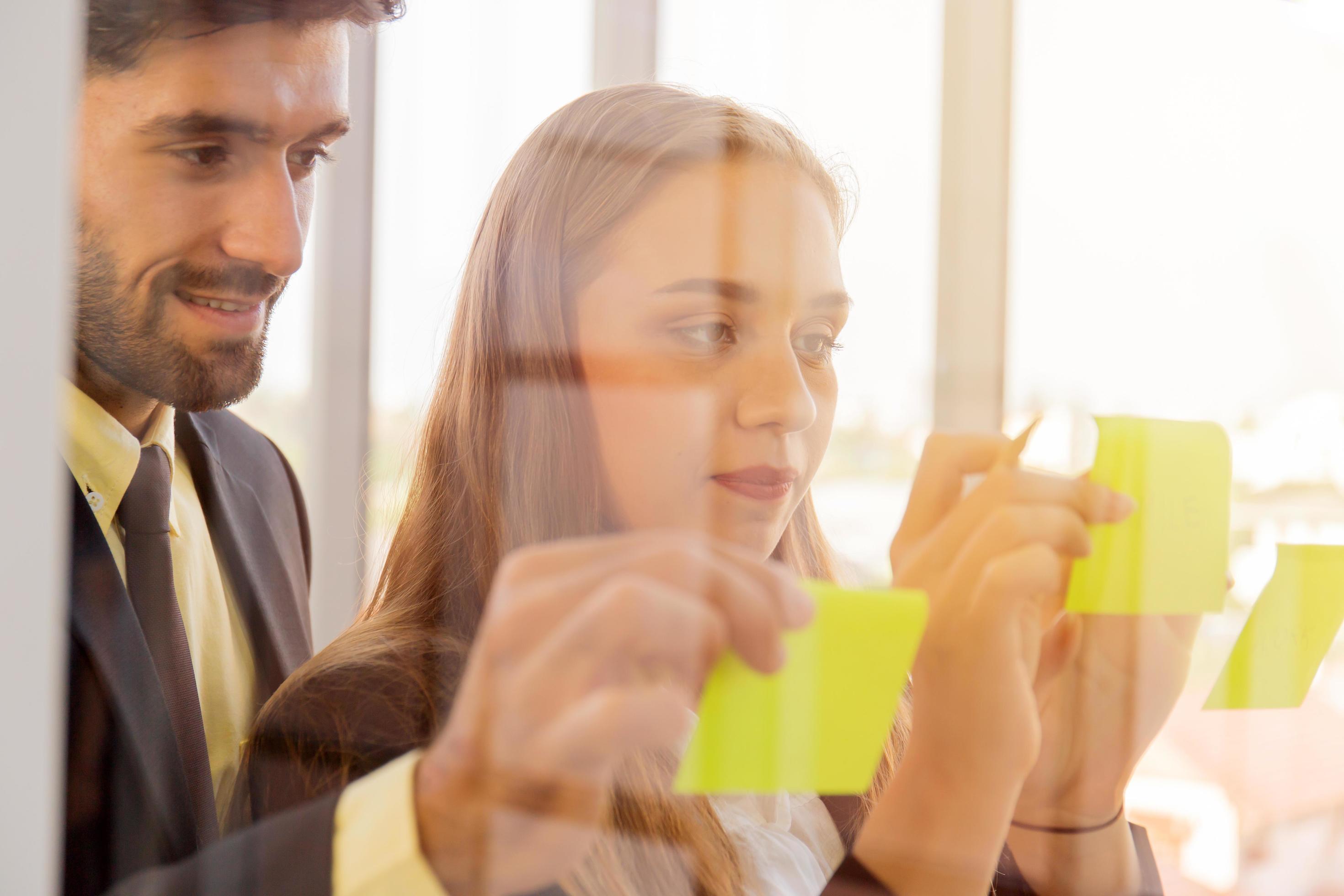 Two business men and women put notes on clear glass and have a beautiful orange light. Stock Free