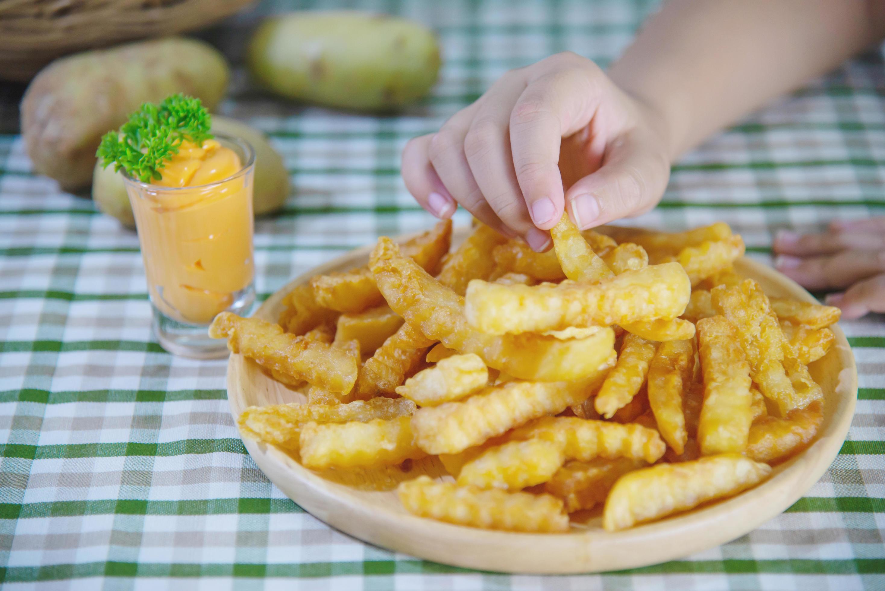 Hand holding delicious fried potato on wooden plate with dipped sauce – traditional fast food concept Stock Free