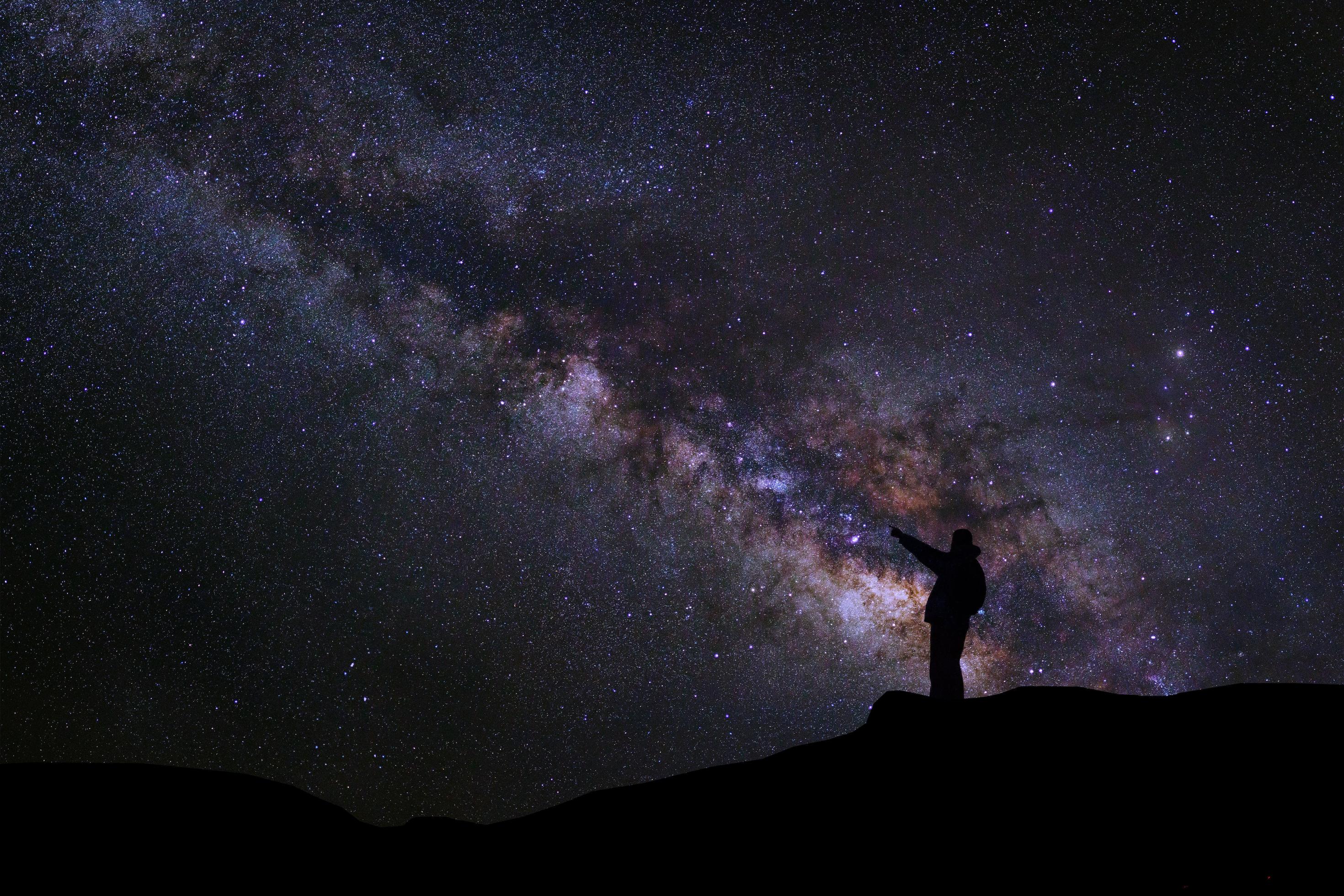 A Man is standing next to the milky way galaxy pointing on a bright star, Long exposure photograph, with grain Stock Free