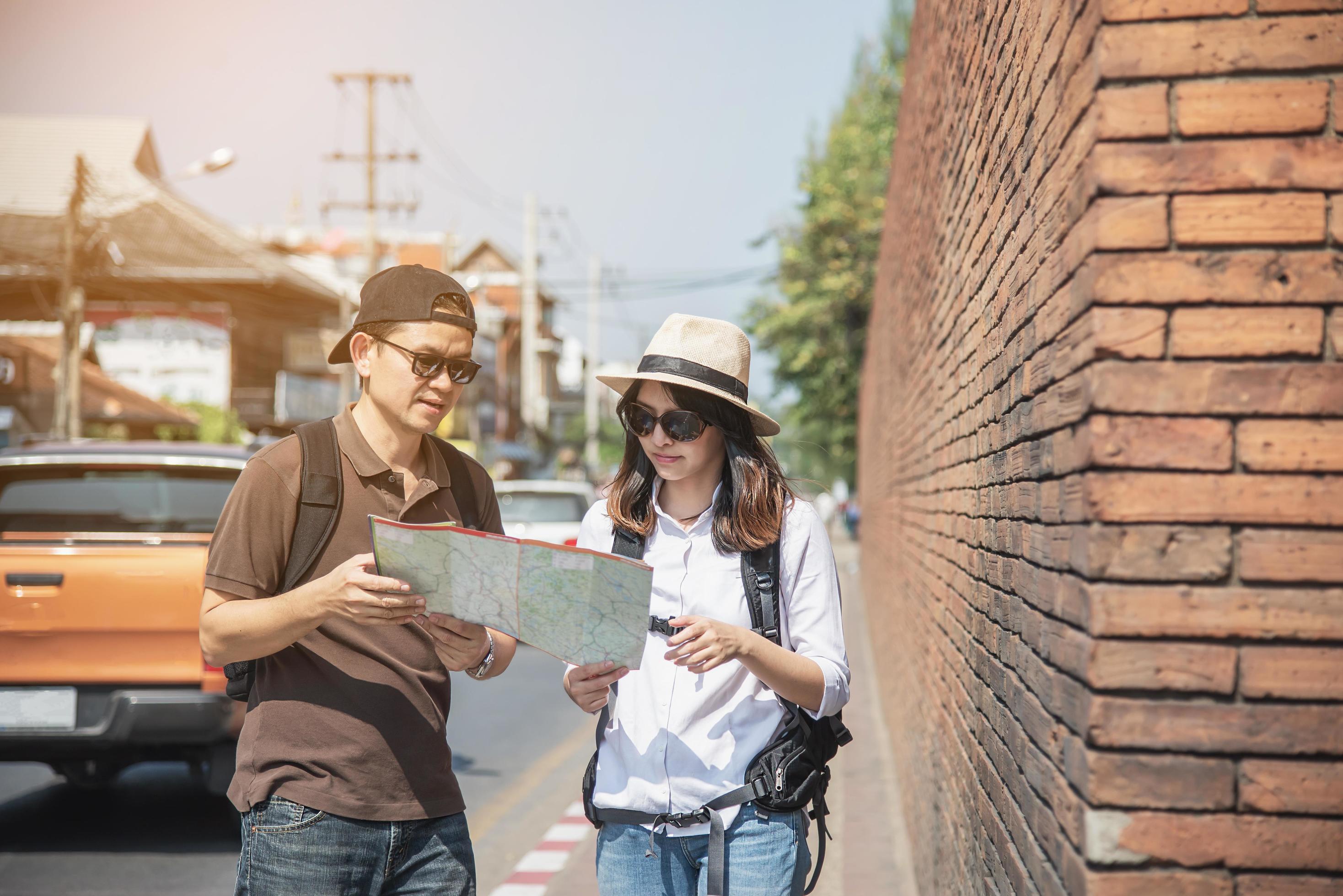 Asian backpack couple tourist holding city map crossing the road – travel people vacation lifestyle concept Stock Free