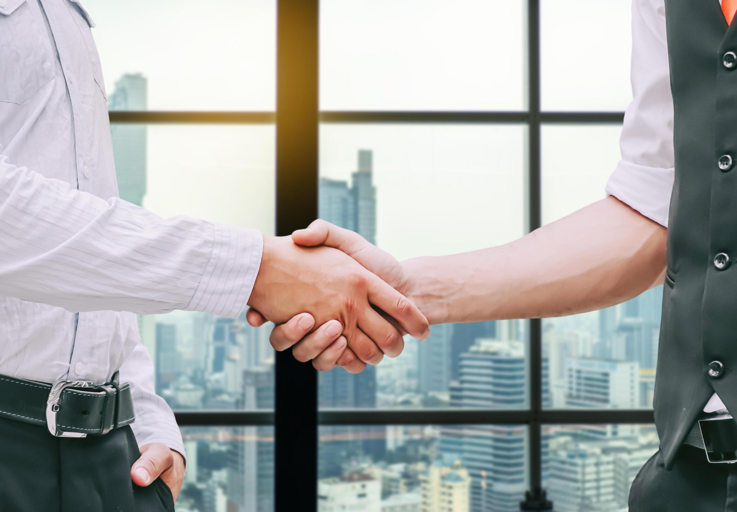 Close up of a business hand shake between two colleagues – greeting, dealing, merger and acquisition concepts on Modern glass building background Stock Free