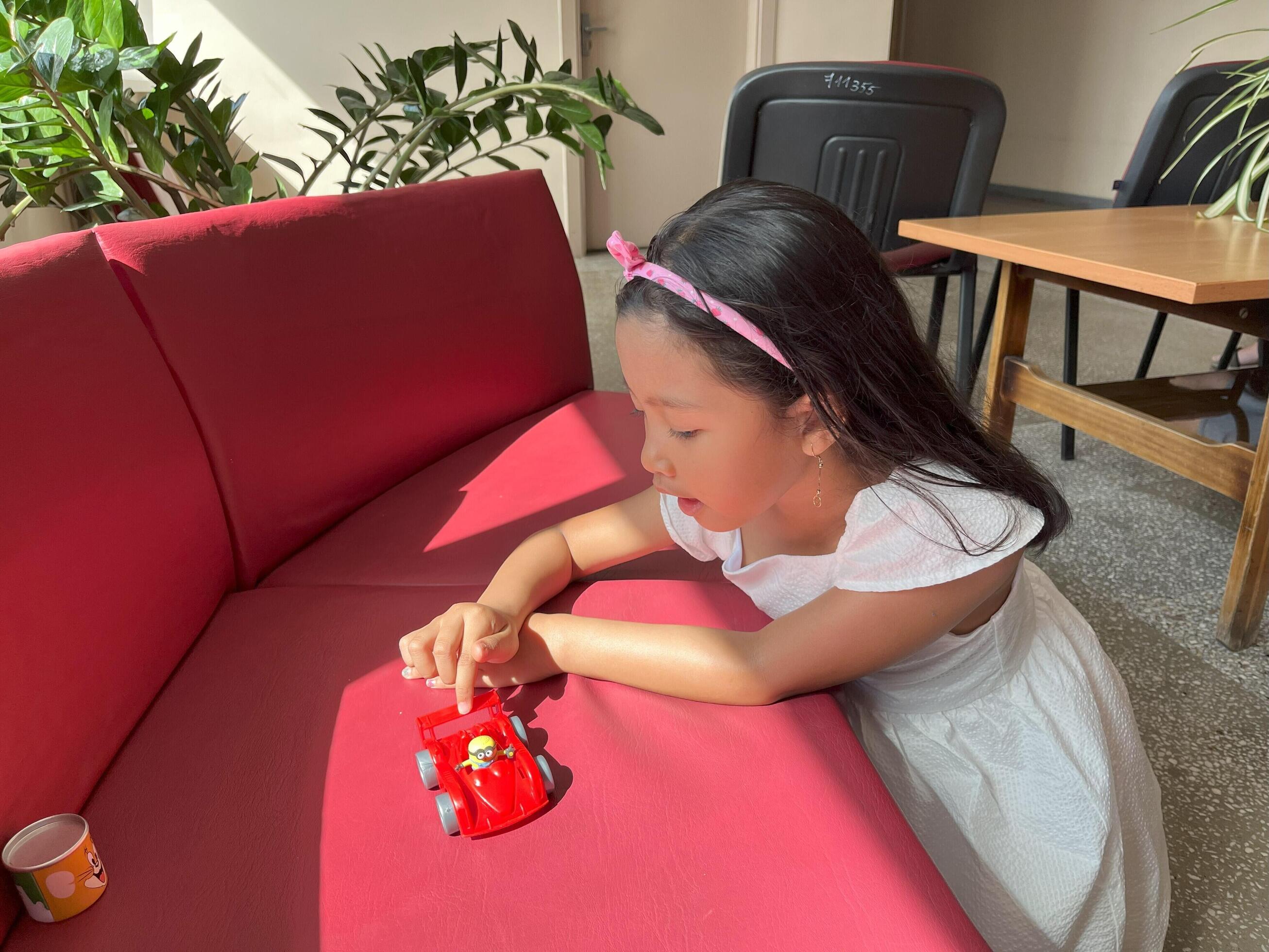 A five year old Asian child plays with her toys in red sofa while waiting in line at the hospital Stock Free