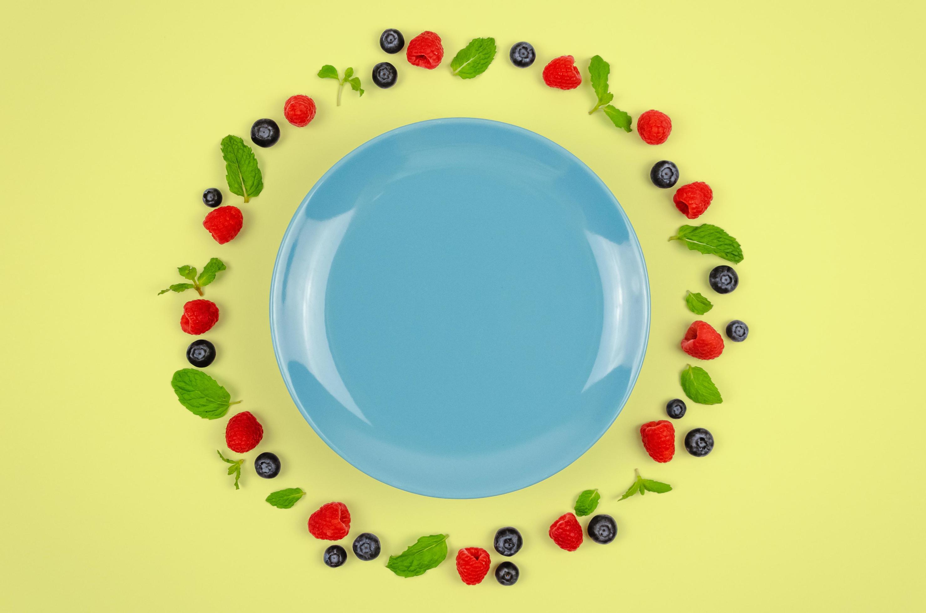 Fresh blueberries, raspberries and mint leaf on top view with blue plate and pastel yellow color background for healthy food concept. Stock Free