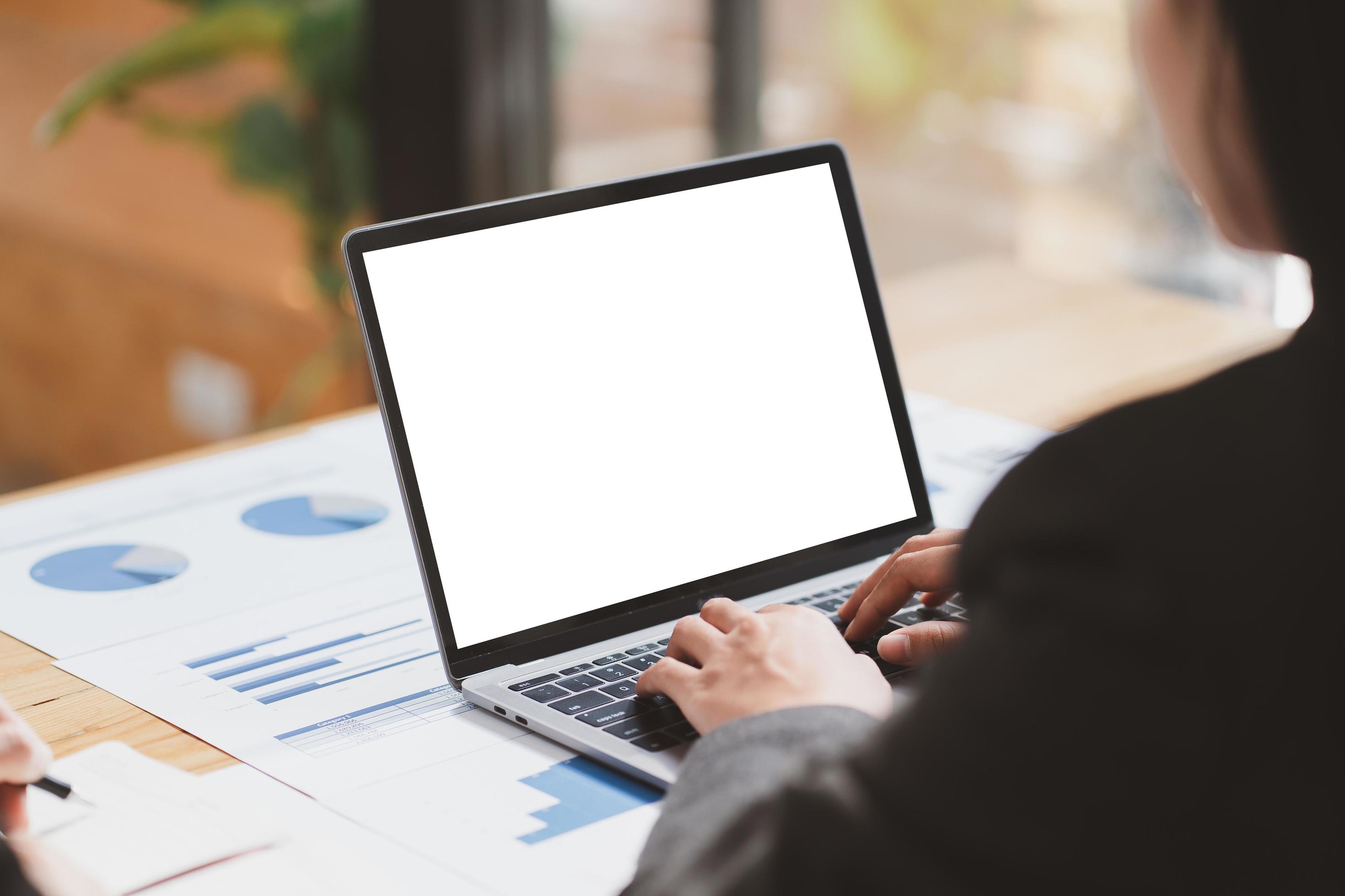 Mockup image of business woman using and typing on laptop with blank white screen and coffee cup on glass table in modern loft cafe Stock Free