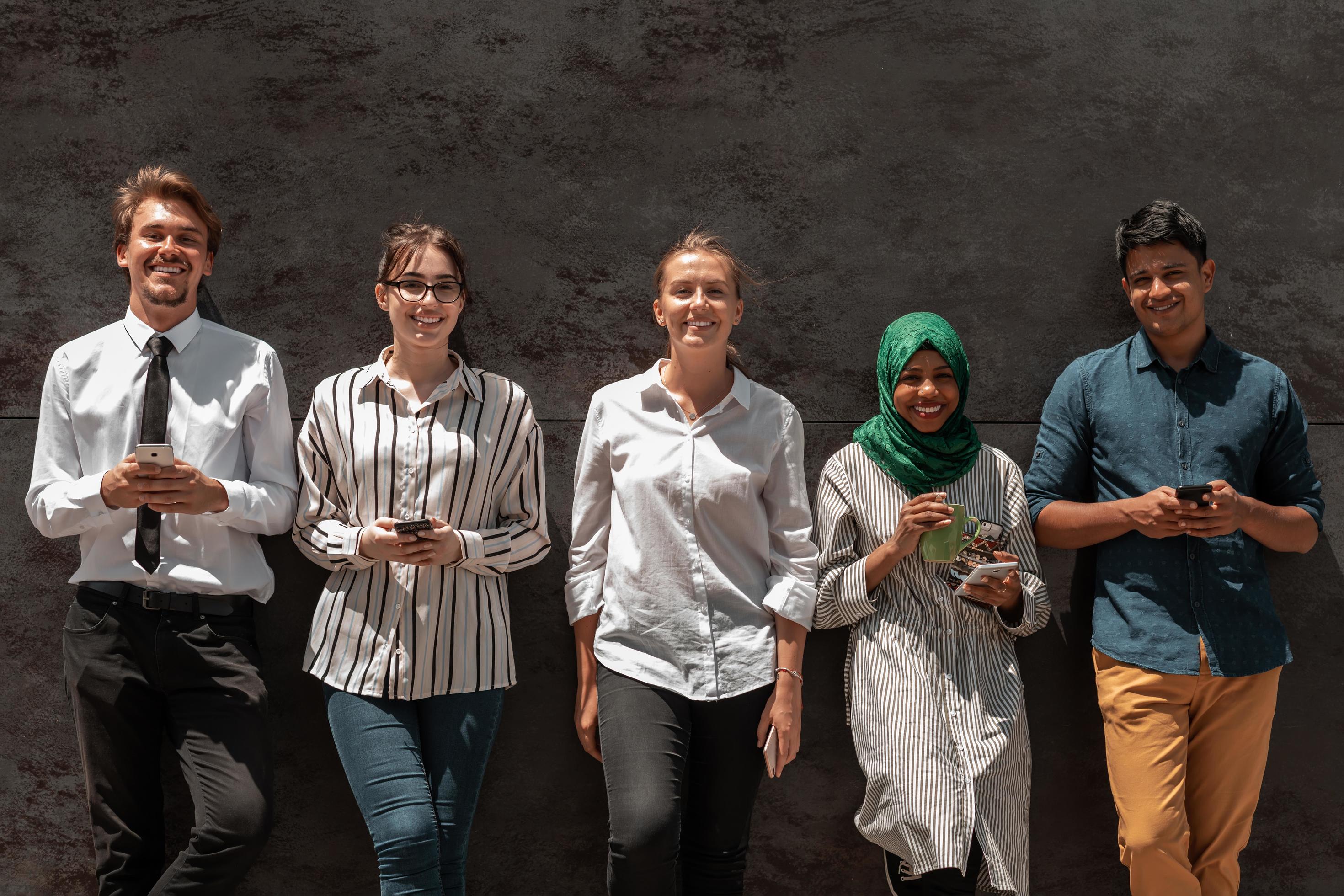 Multiethnic group of casual business people using mobile phone during coffee break from work in front of black wall outside Stock Free