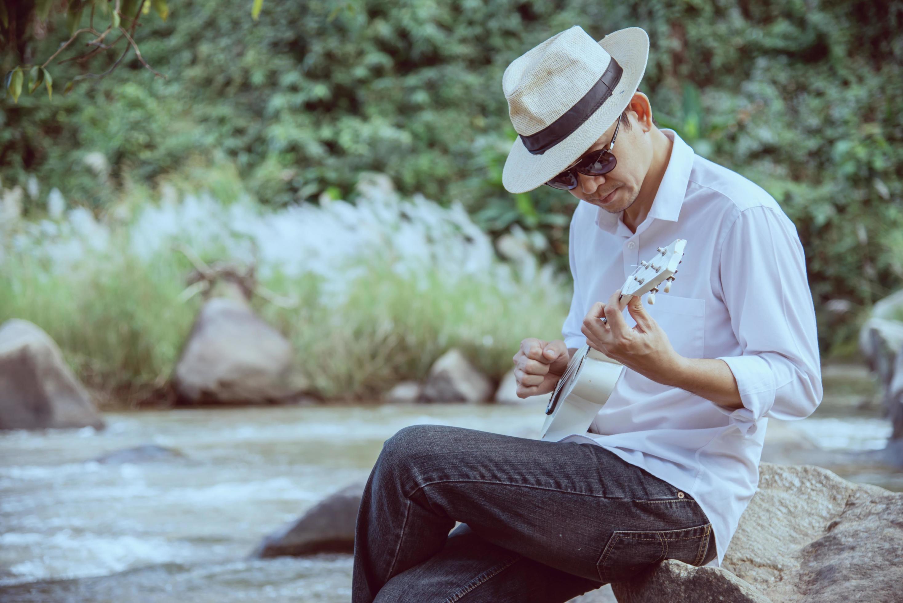 Man play ukulele new to the river- people and music instrument life style in nature concept Stock Free