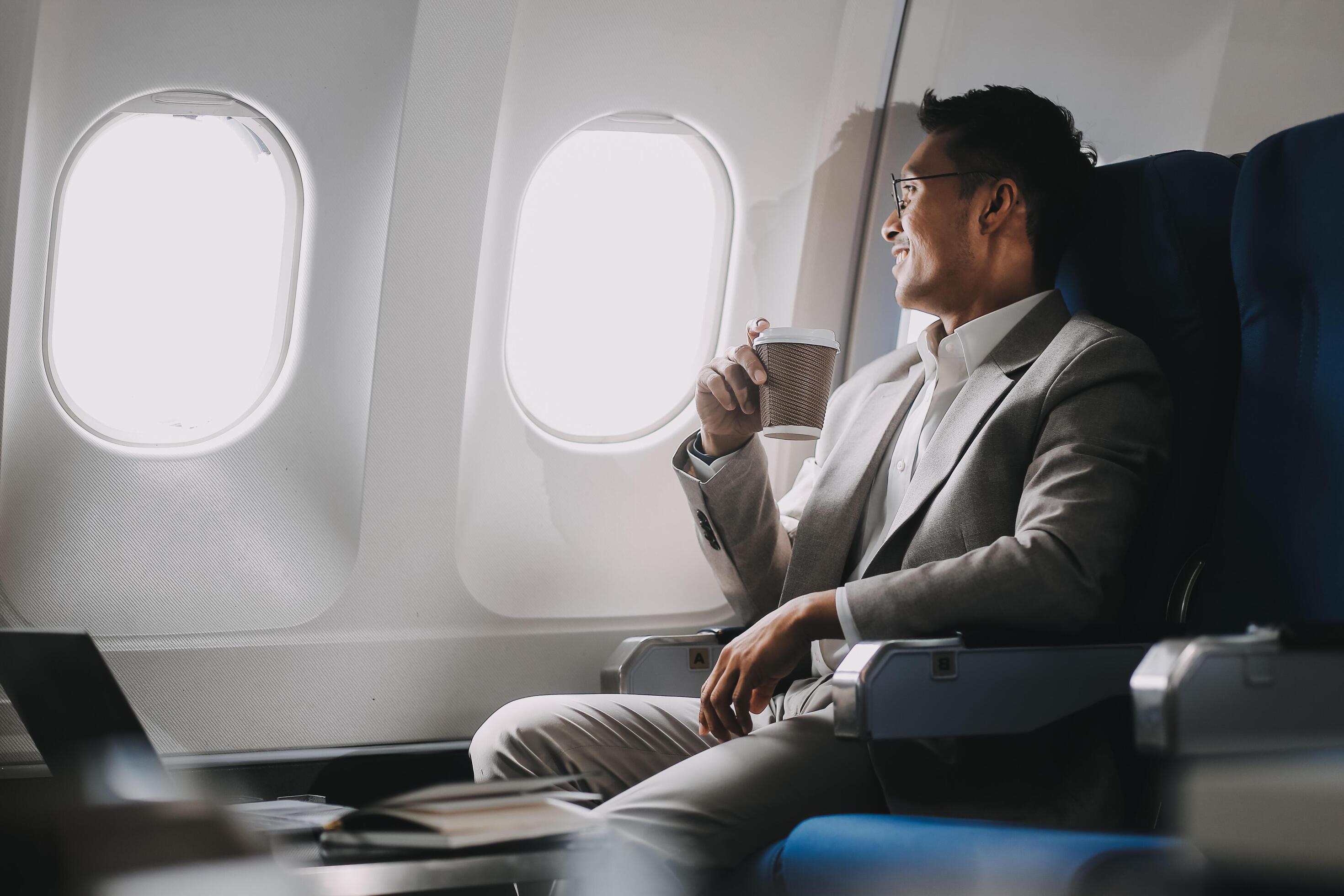 Asian businessman enjoying enjoys a coffee comfortable flight while sitting in the airplane cabin, Passengers near the window. Stock Free