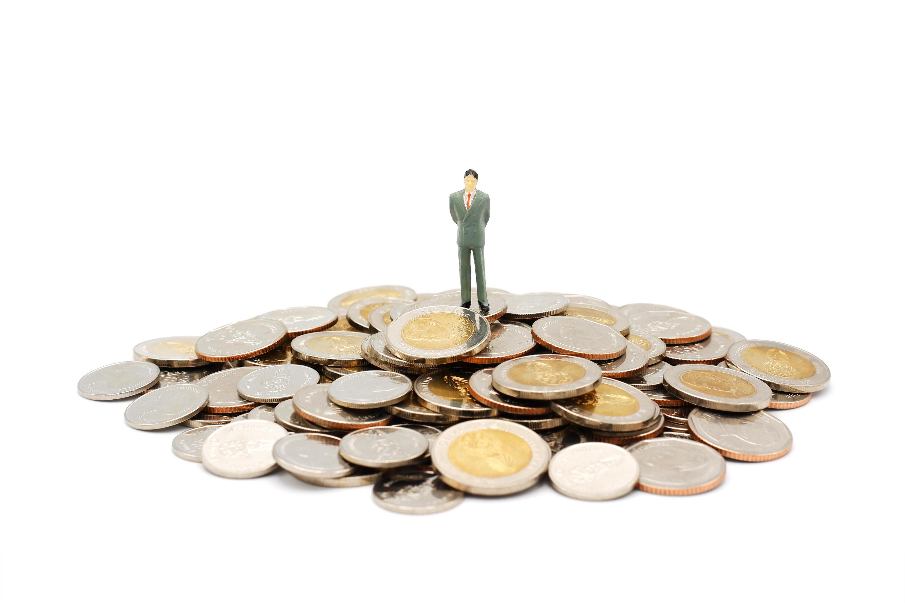 Miniature businessman standing on pile of new Thai Baht coins, isolated on white background. Business and finance concept. Stock Free