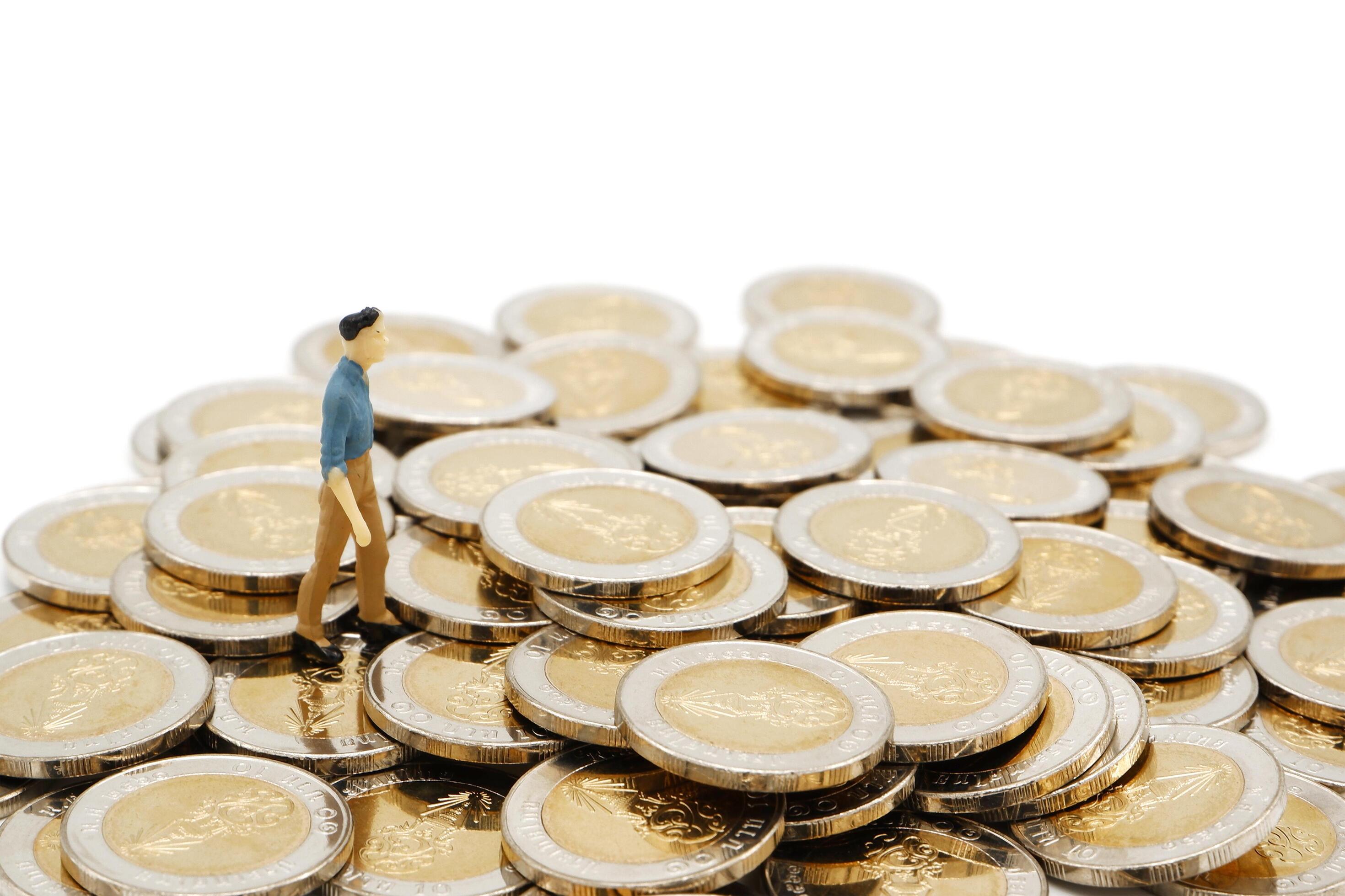 Miniature businessman standing on pile of new 10 Thai Baht coins, isolated on white background. Business concept. Stock Free