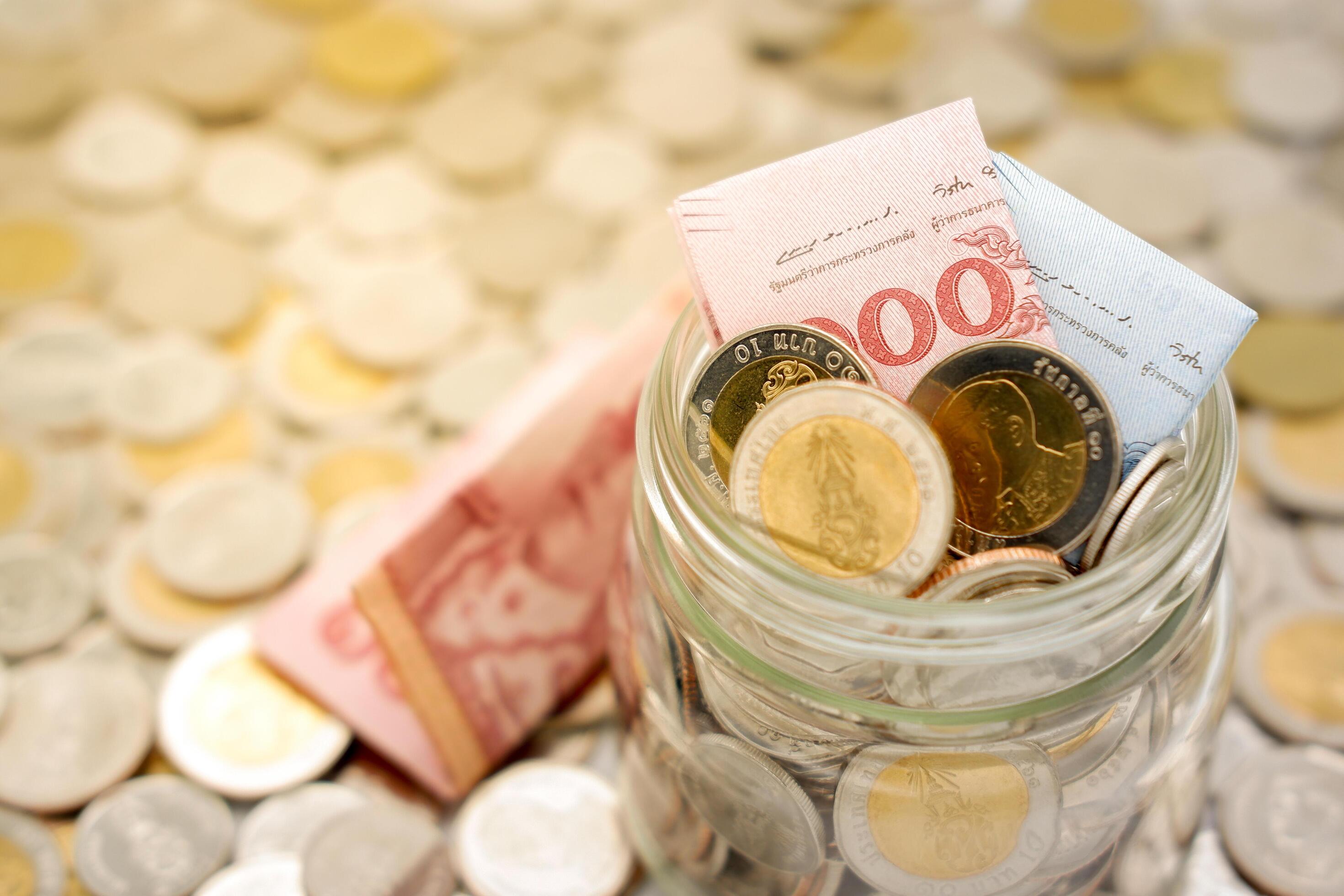 Close-up image of a glass jar full of new Thai baht banknotes and coins. Business and finance concept. Stock Free