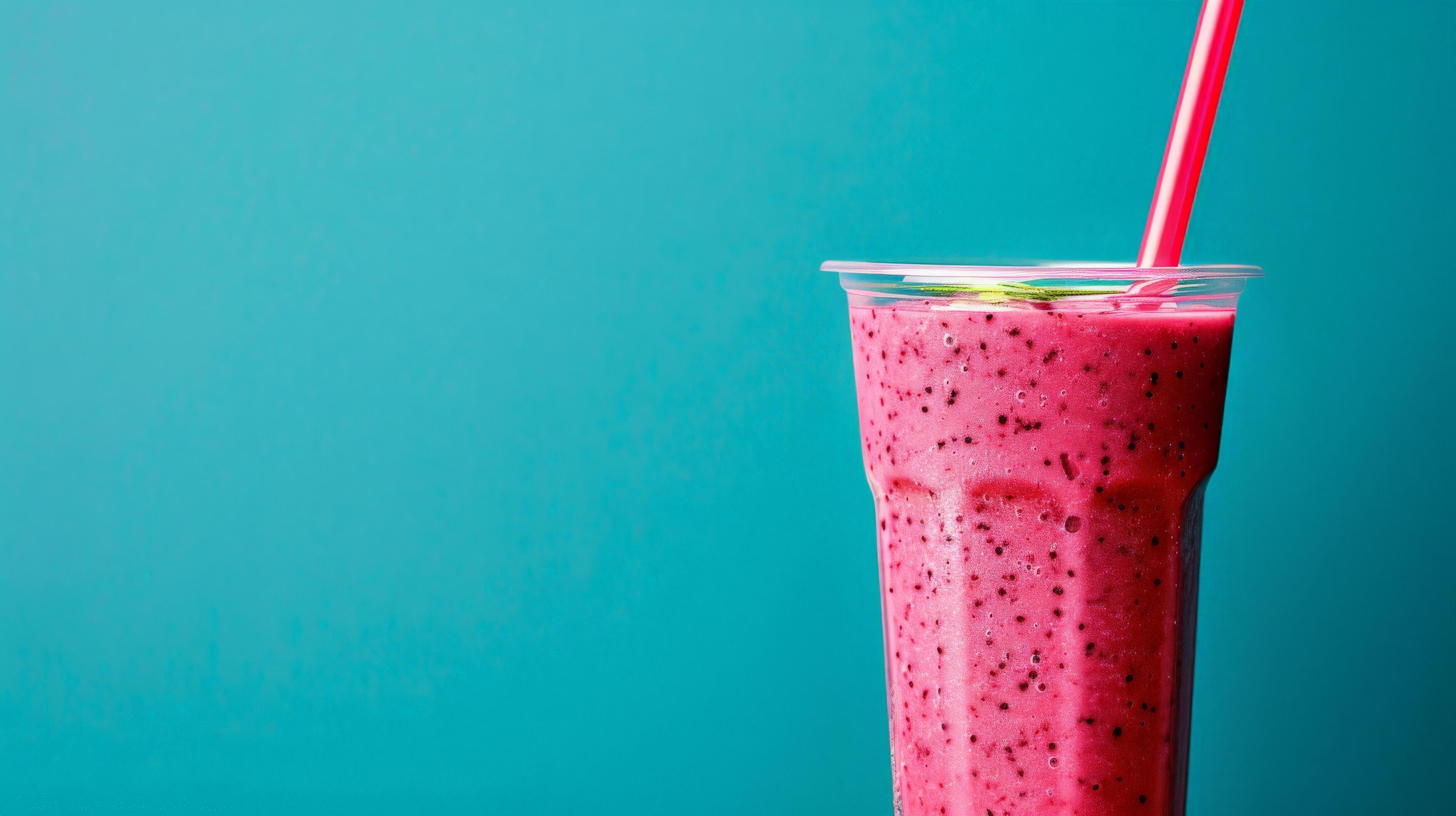 A glass of pink smoothie with a straw sits against a vibrant blue background Stock Free