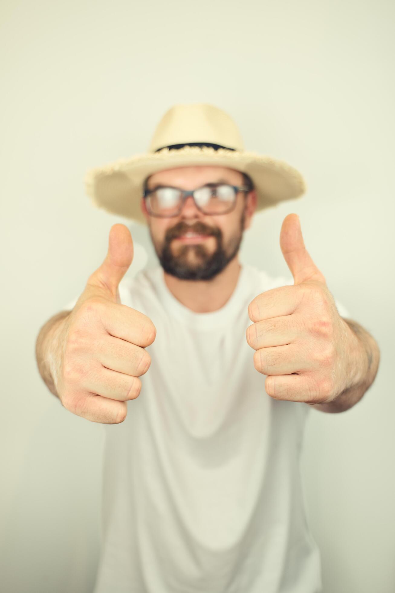 portrait of handsome bearded man with straw hat and glasses smiling, thumbs up gesture, wearing white shirt , isolated on white background Stock Free