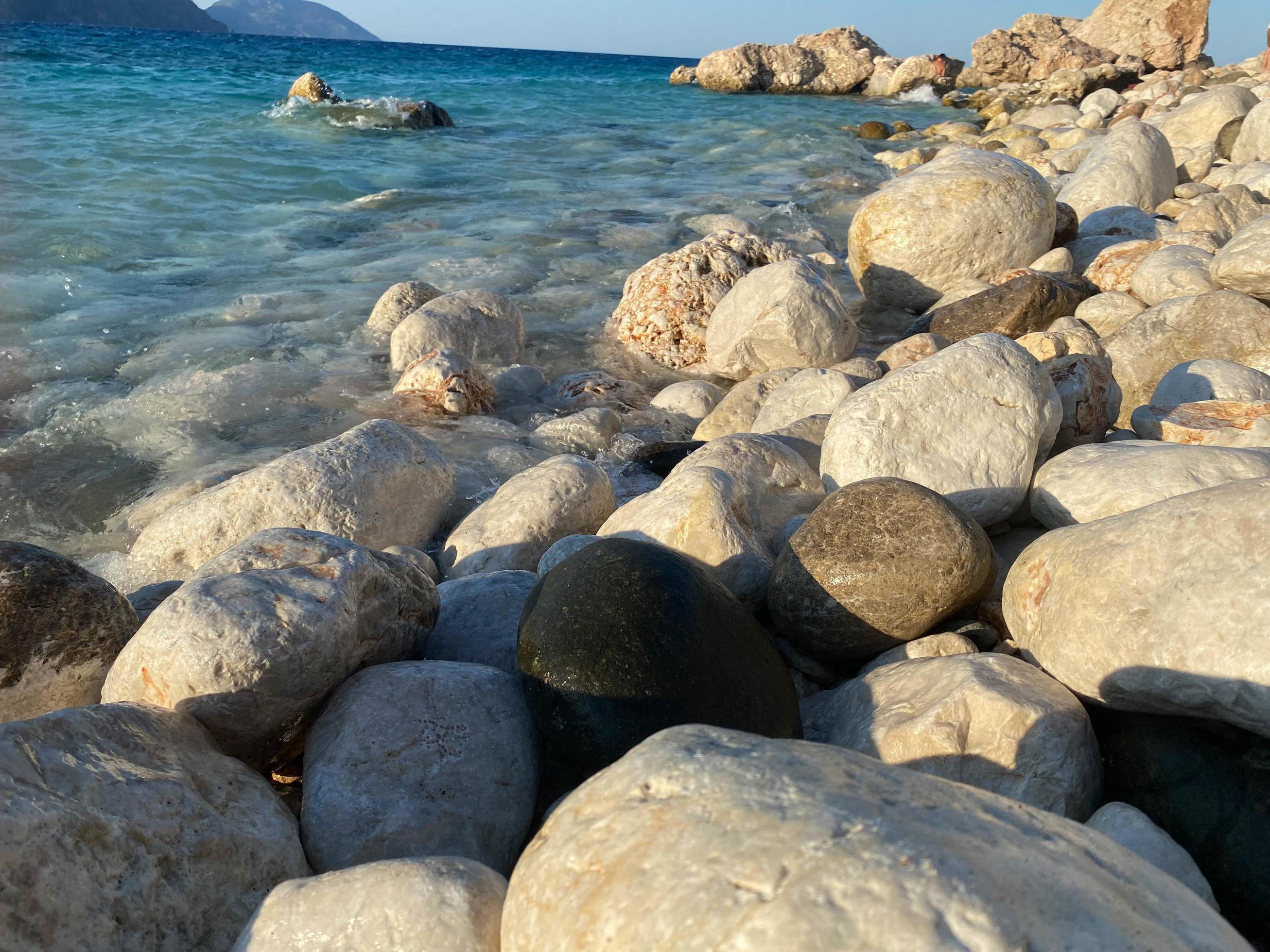 Large beautiful natural round stones and pebbles washed by water on the seashore or ocean against the backdrop of mountains Stock Free