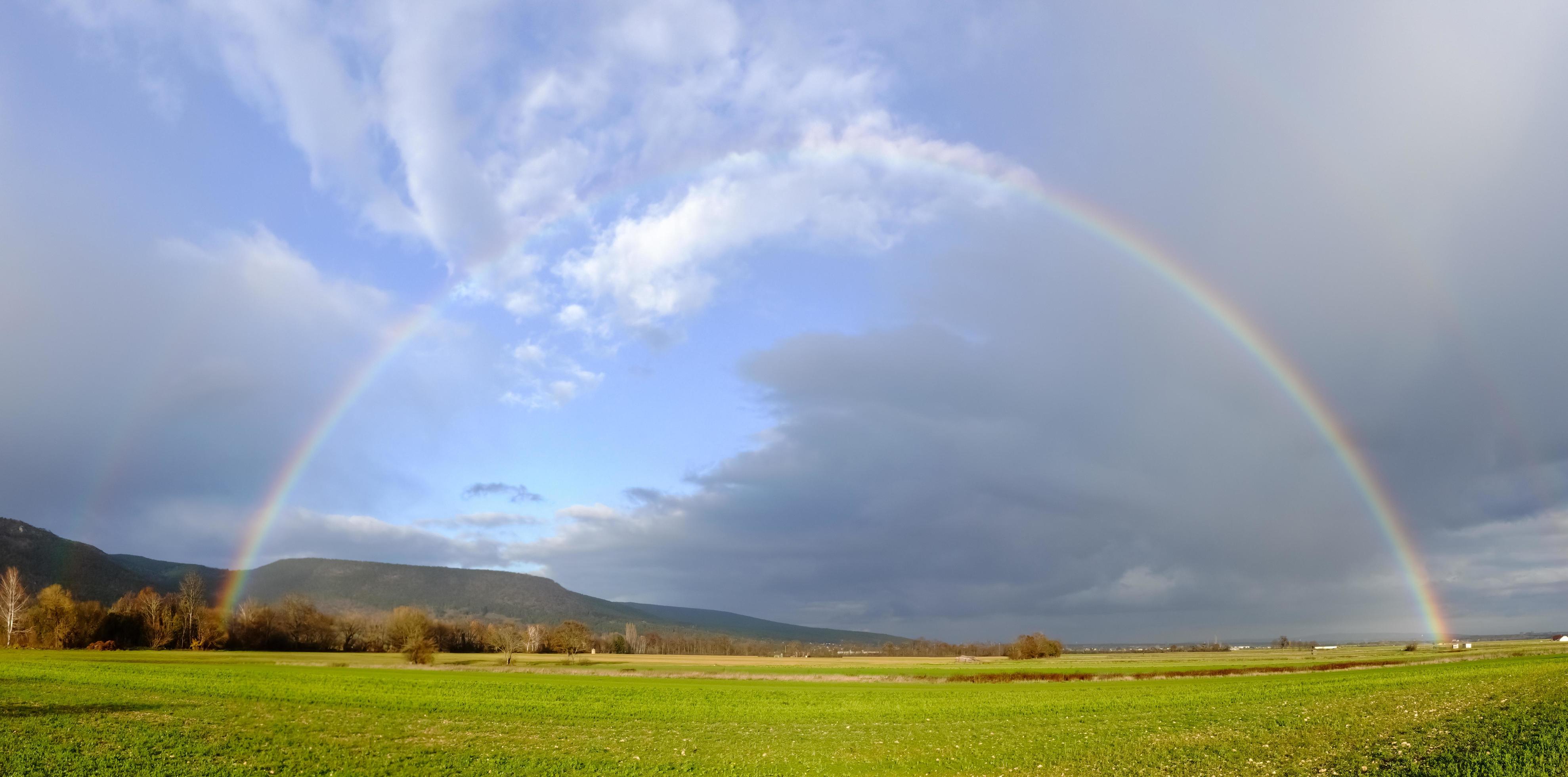 rainbow on dark rain clouds over green fields in the winter panorama Stock Free