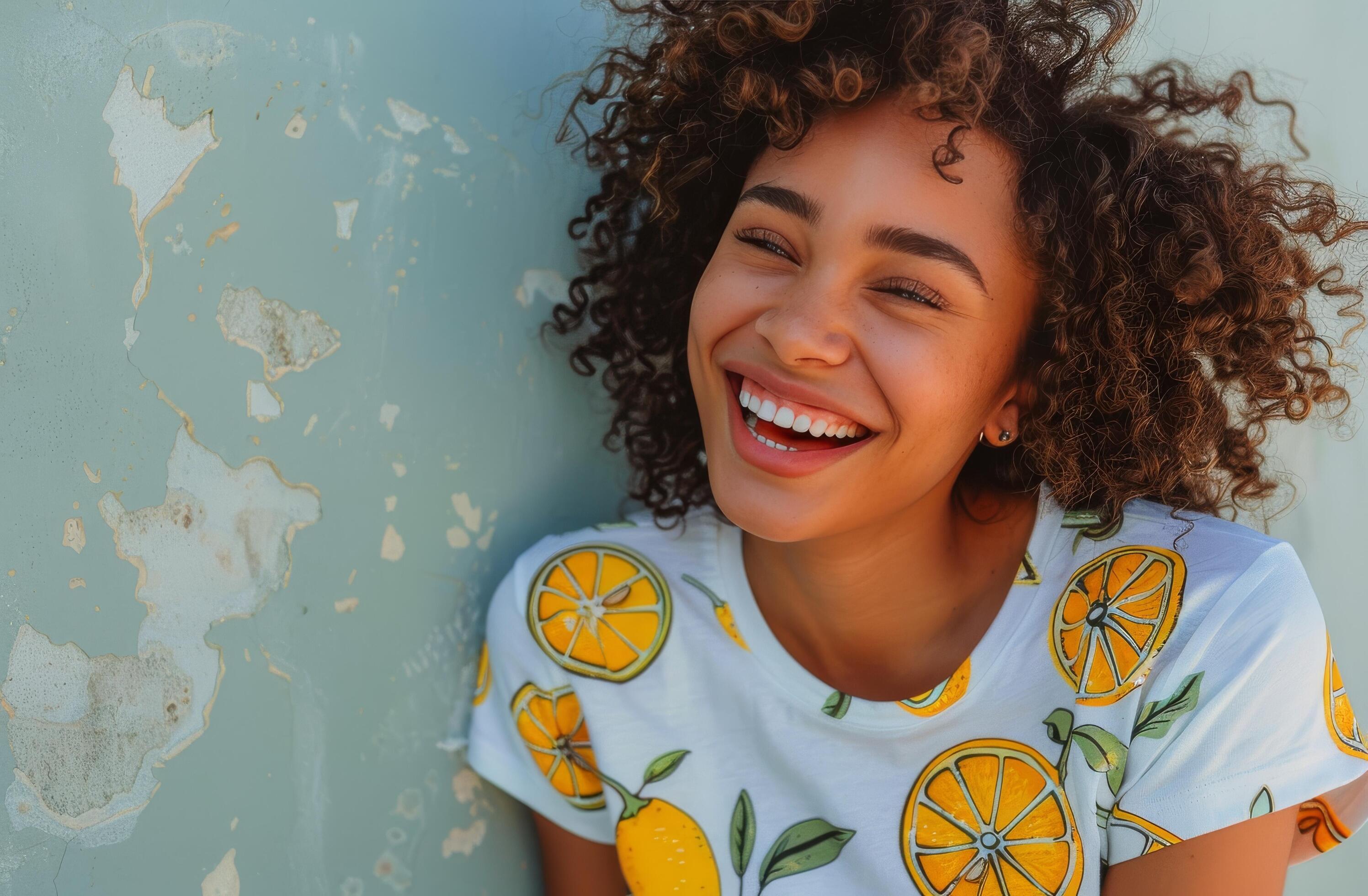 Woman With Curly Hair Smiles Against a Green Wall While Wearing a Lemon-Patterned Shirt Stock Free