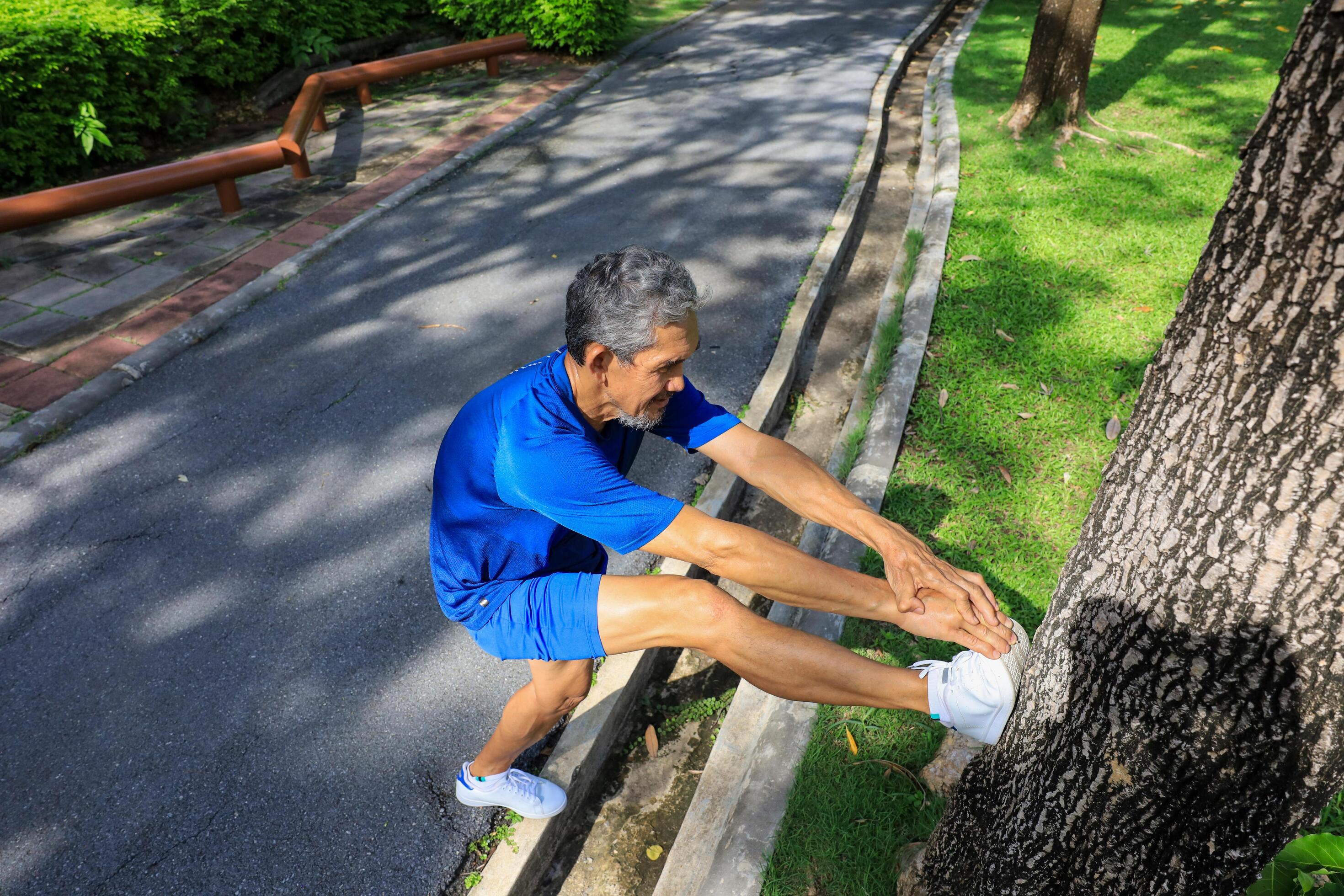 Senior Asian man is stretching his leg muscle during warm up exercise work out in the morning at public park for healthy and longevity concept Stock Free