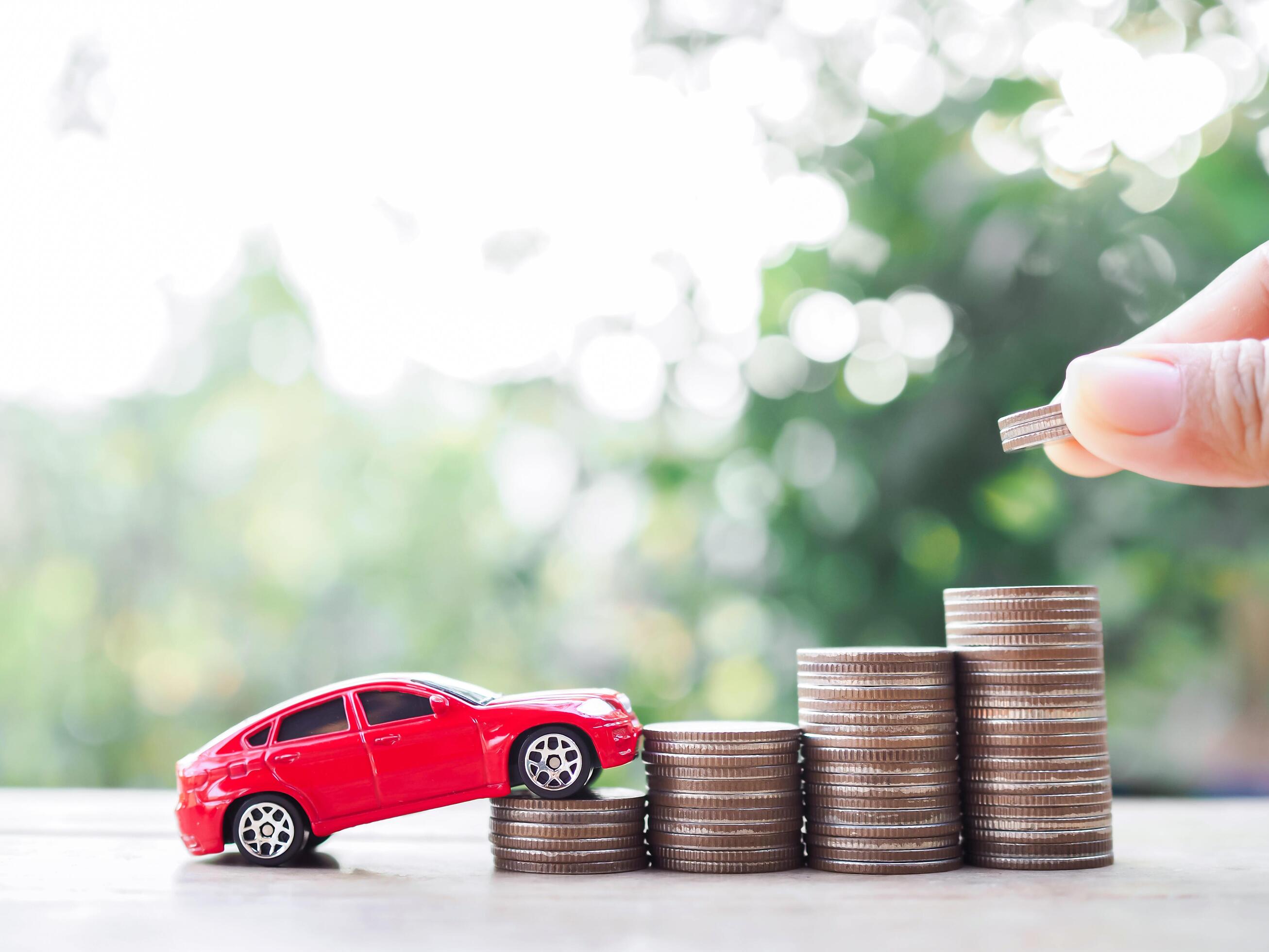 Close up hand putting coins into stack of coins amd toy car. The concept of saving money and manage to success transport business Stock Free