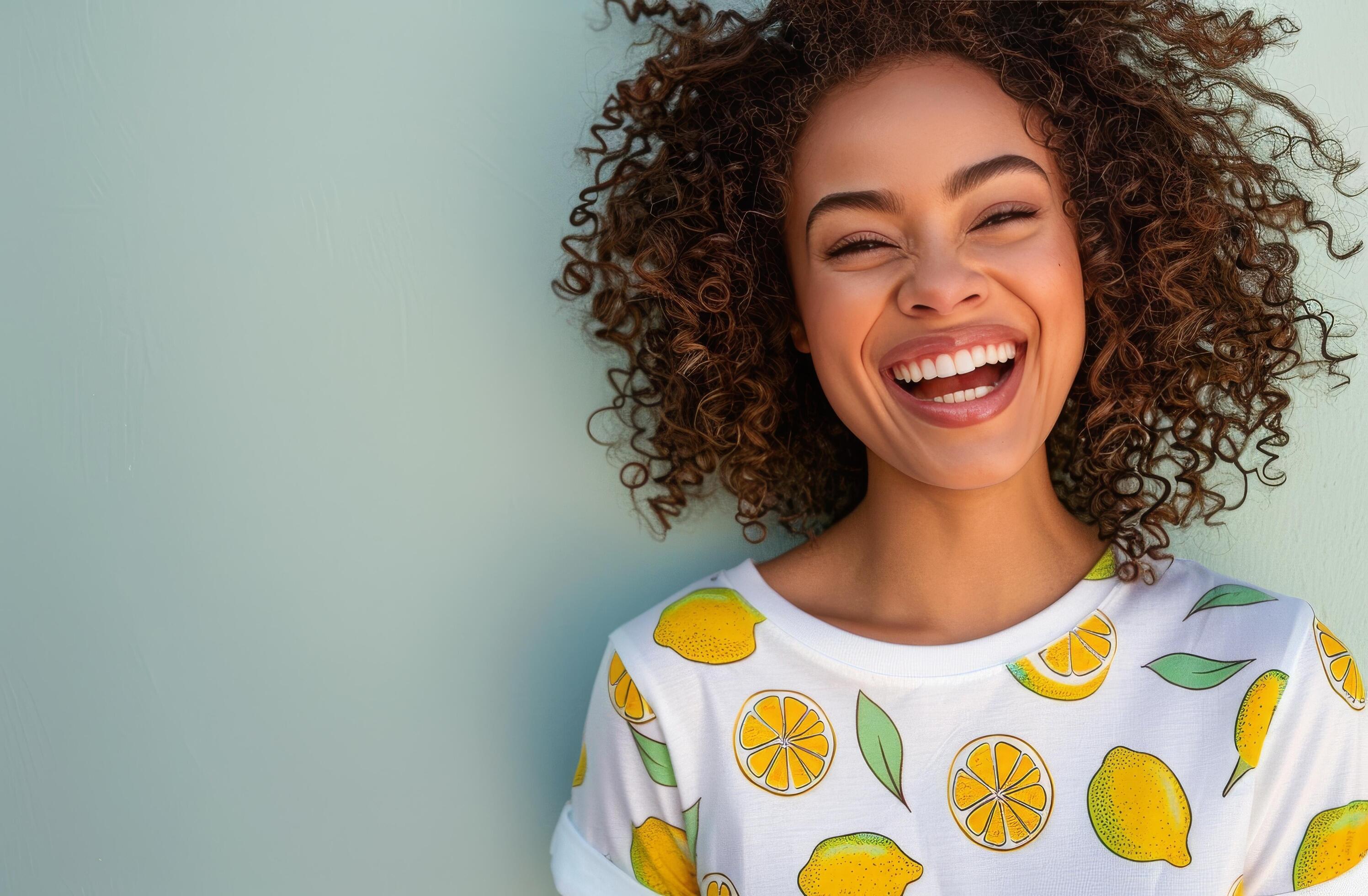 Woman With Curly Hair Smiles Against a Green Wall While Wearing a Lemon-Patterned Shirt Stock Free