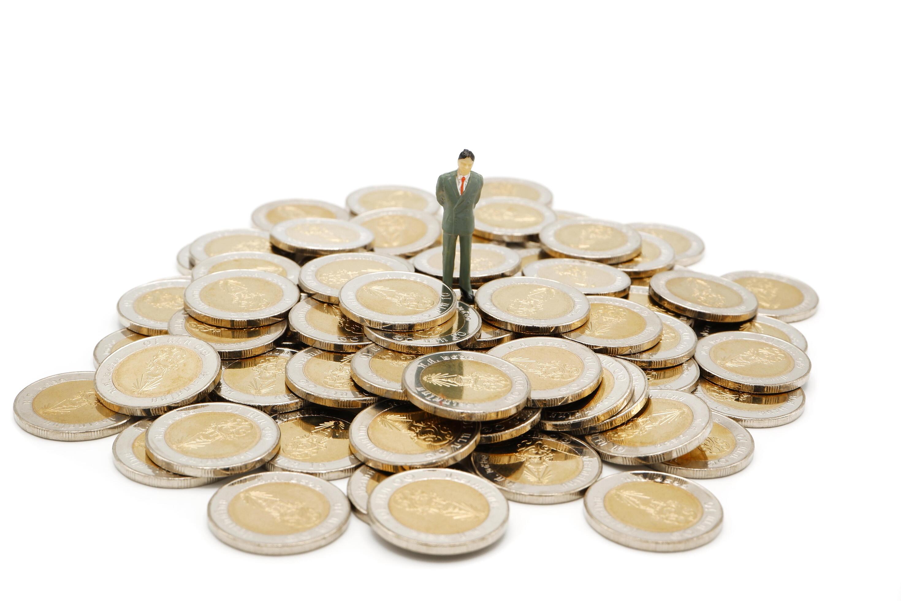 Miniature businessman standing on pile of new 10 Thai Baht coins, isolated on white background. Business concept. Stock Free